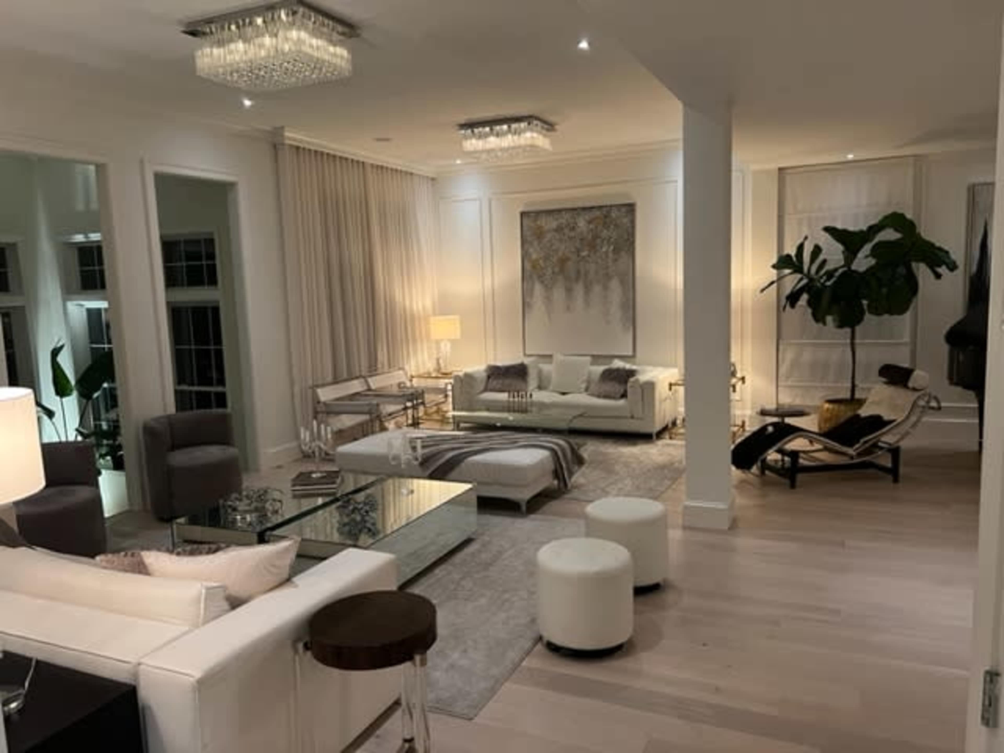 A modern living room with white furniture, large windows, and elegant decor, featuring a mix of seating areas and a low coffee table.