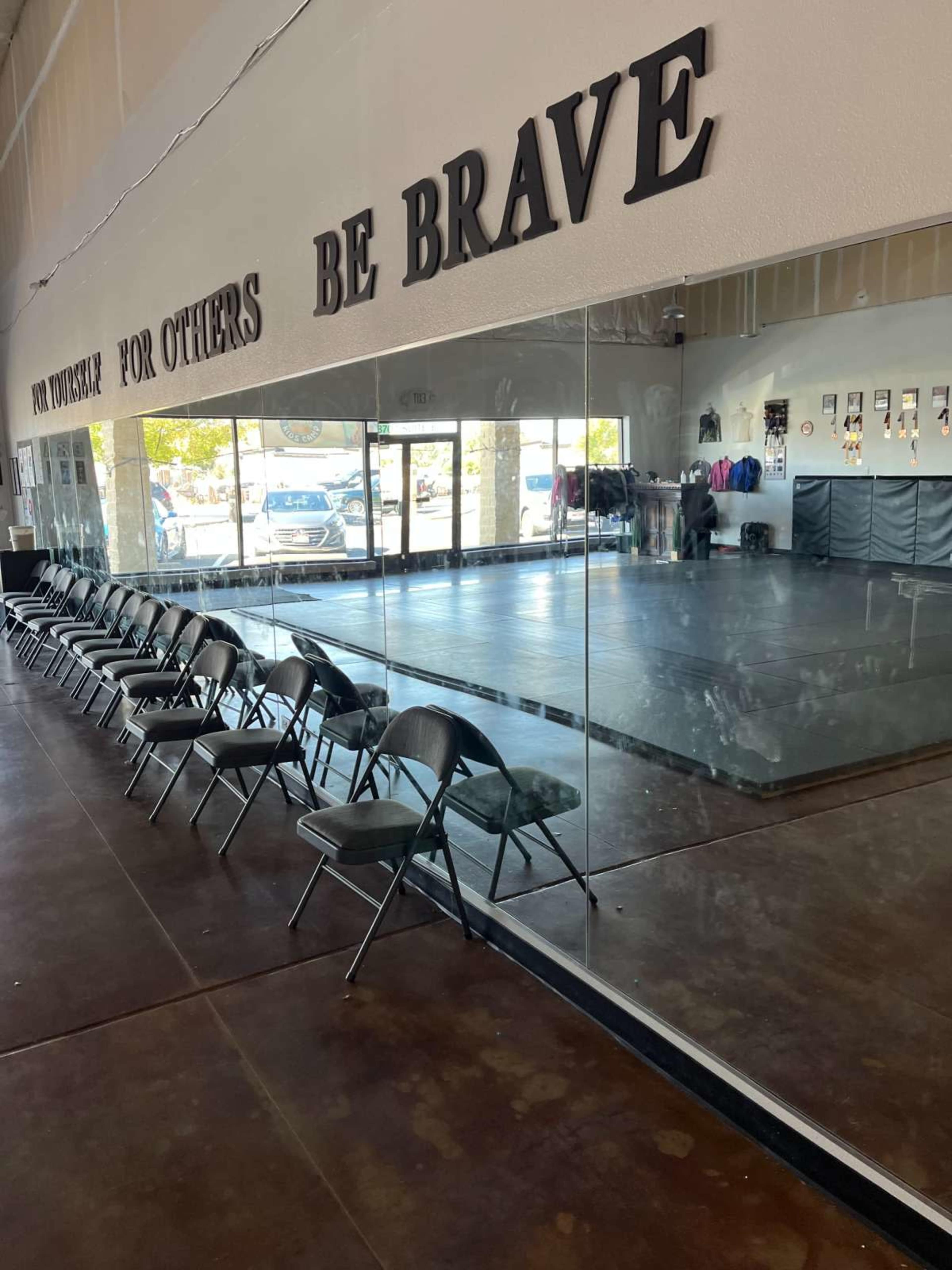 The image shows a dance studio with a large mirror, black chairs arranged in a row, and a wooden floor.