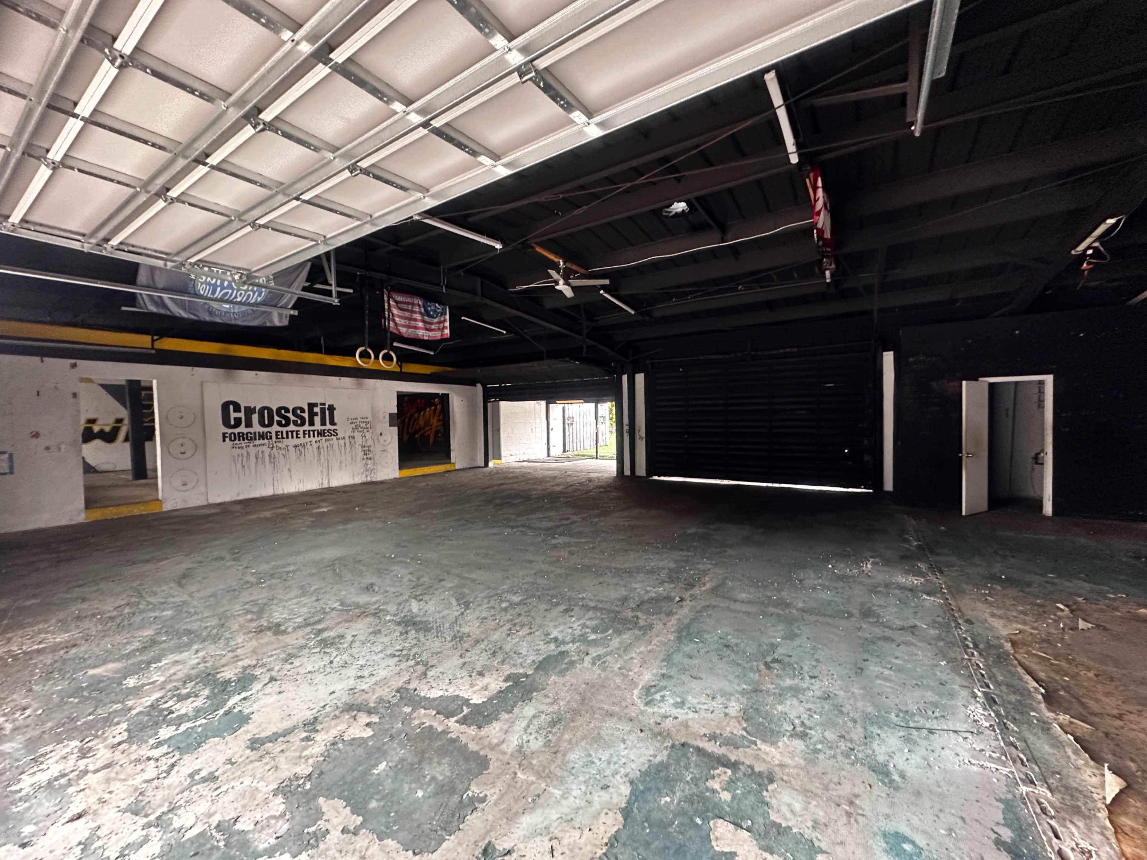 An empty CrossFit gym with a concrete floor and large, open garage doors.