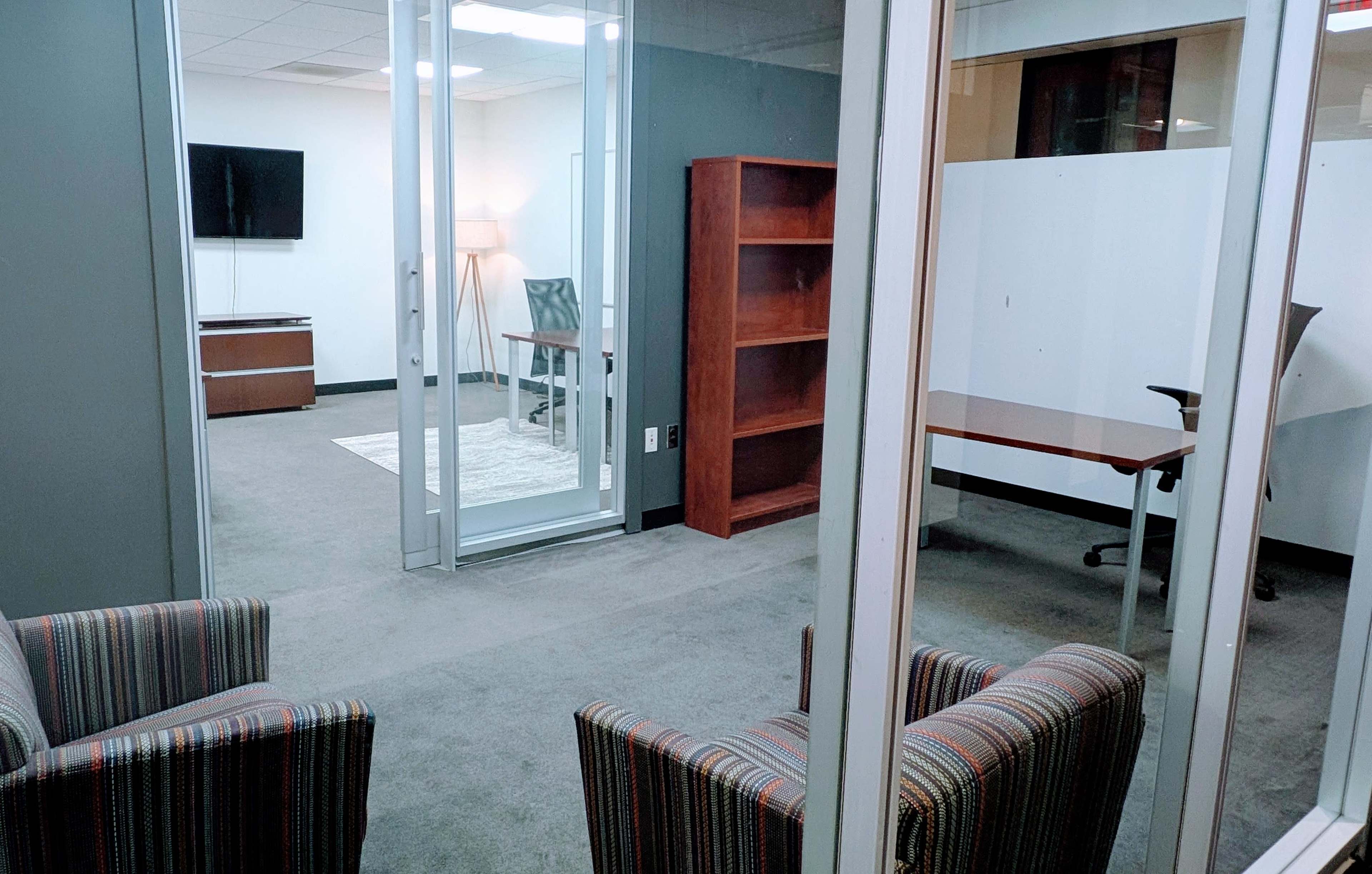 The image shows an office space featuring two striped chairs, a desk, a bookshelf, and a lamp in separate sections of the room.