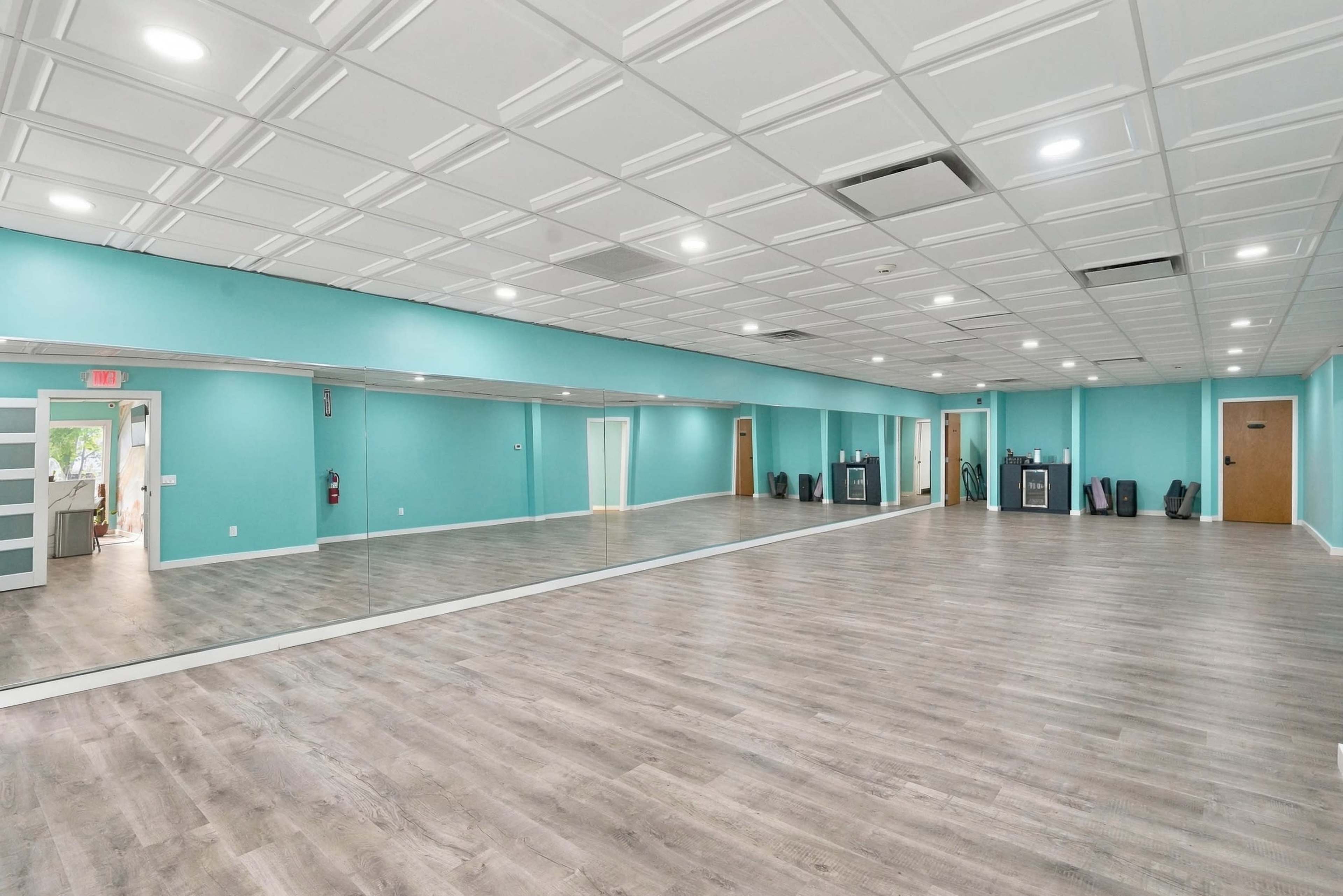 The image shows a spacious room with turquoise walls, a large mirror along one side, and a wooden floor.