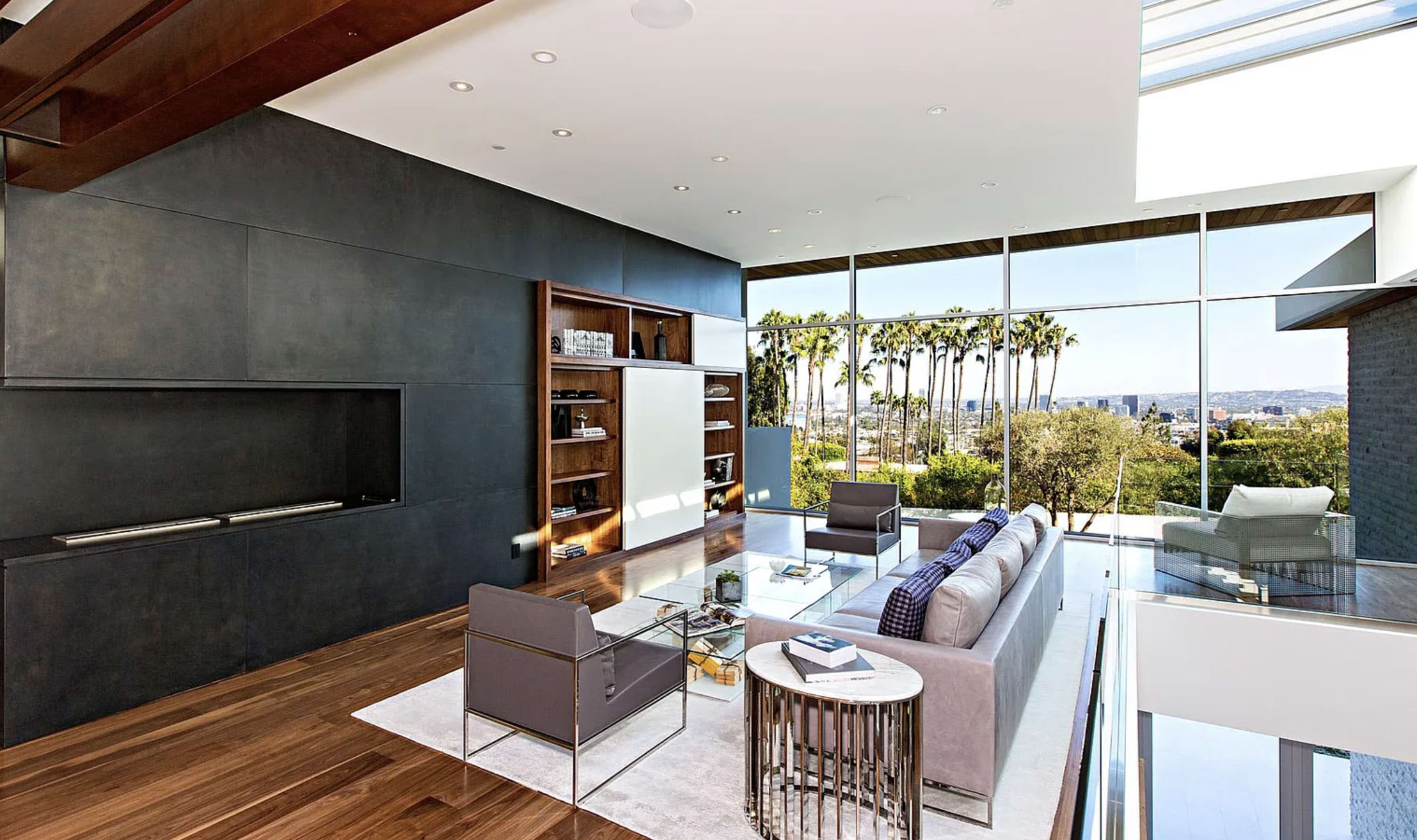 A modern living room features a sleek design with large windows offering a view of palm trees outside.