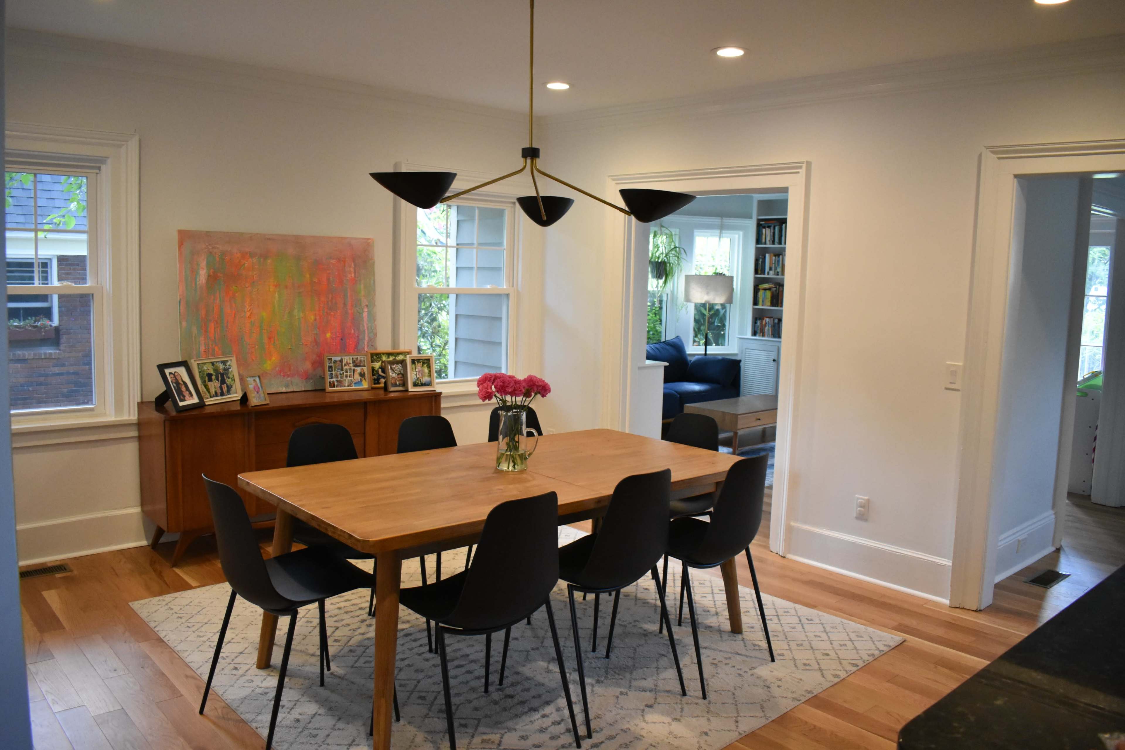 A modern dining room features a wooden table surrounded by six black chairs, with a floral centerpiece and art on the wall.