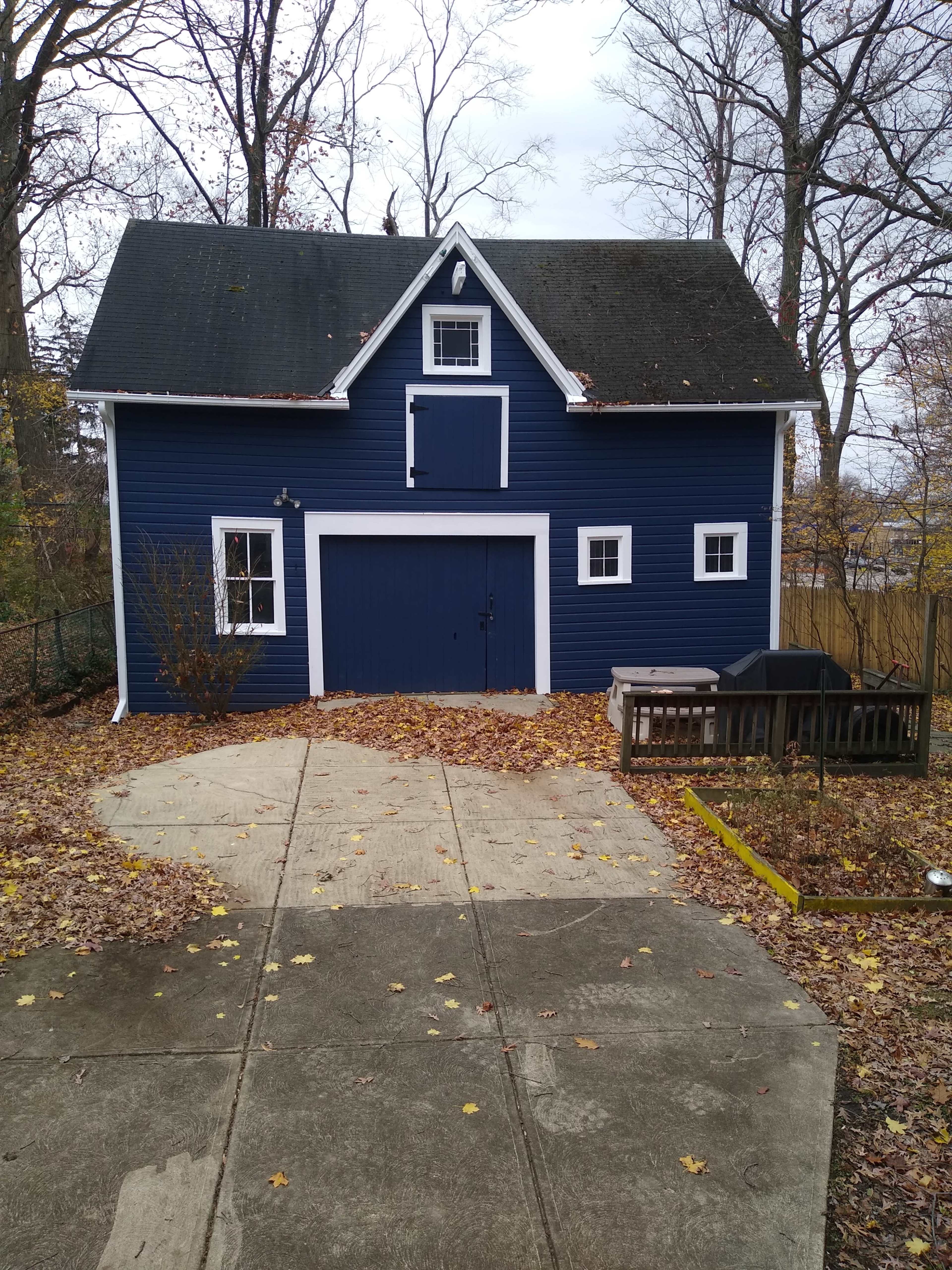 The image shows a blue barn-style shed surrounded by fallen leaves and a concrete driveway.