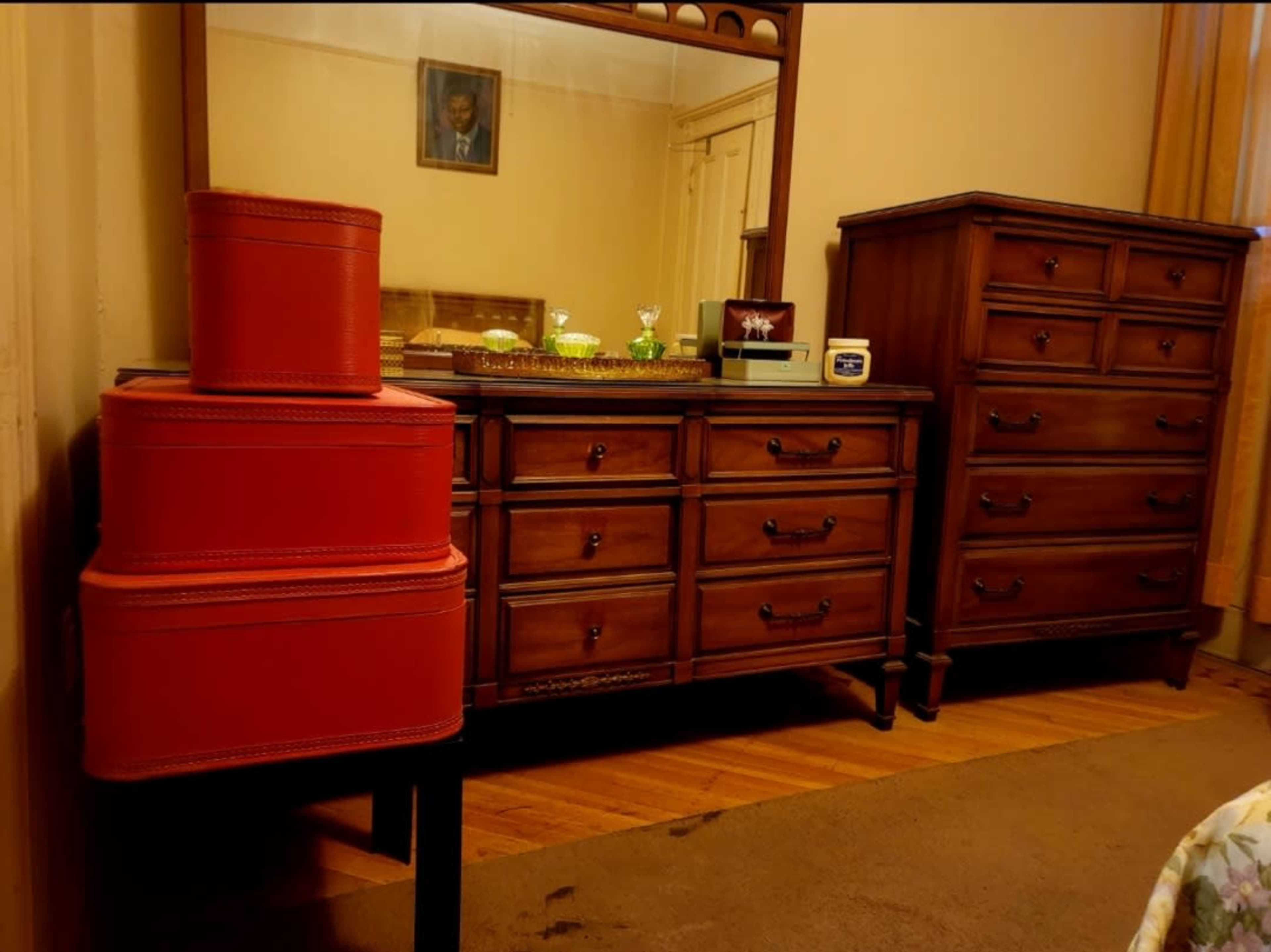 The image shows a room with wooden furniture, including a dresser and a chest of drawers, alongside two stacked red storage boxes.