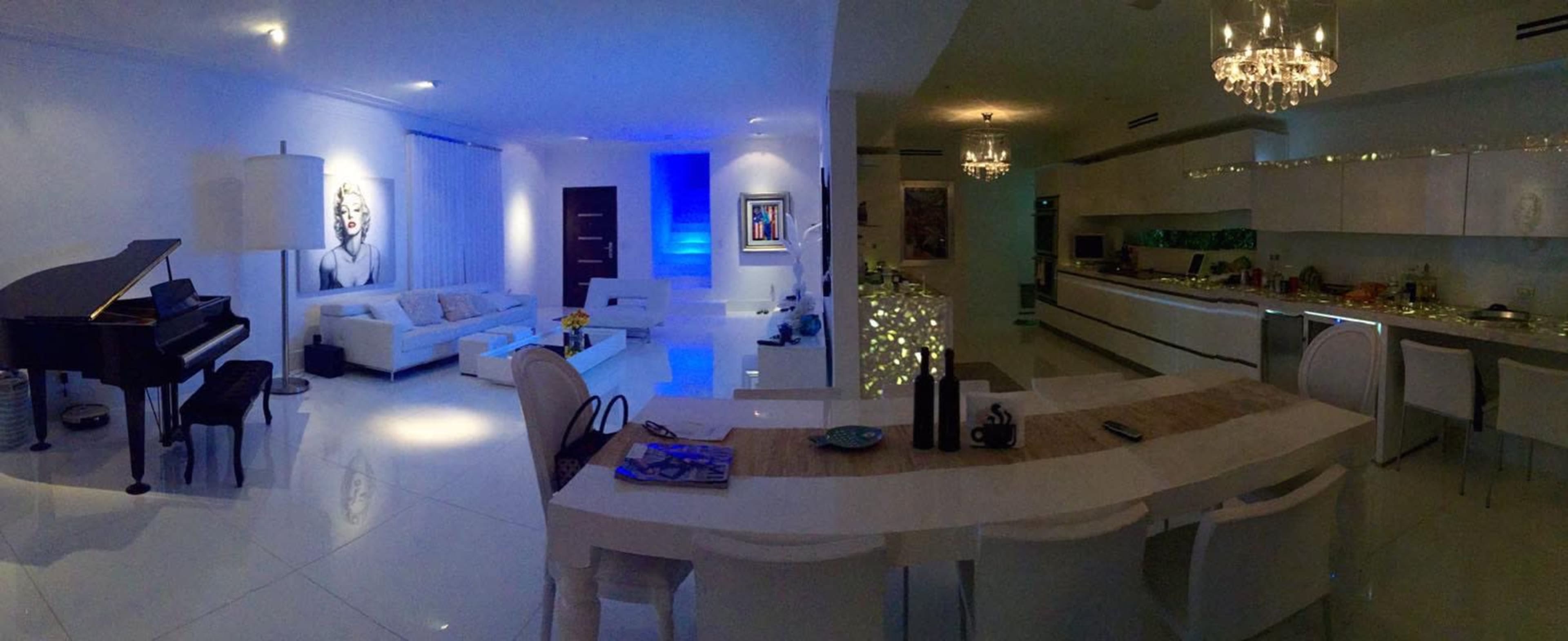 A modern, elegantly designed living space with a grand piano, contemporary furniture, and ambient lighting, leading into an open kitchen area.