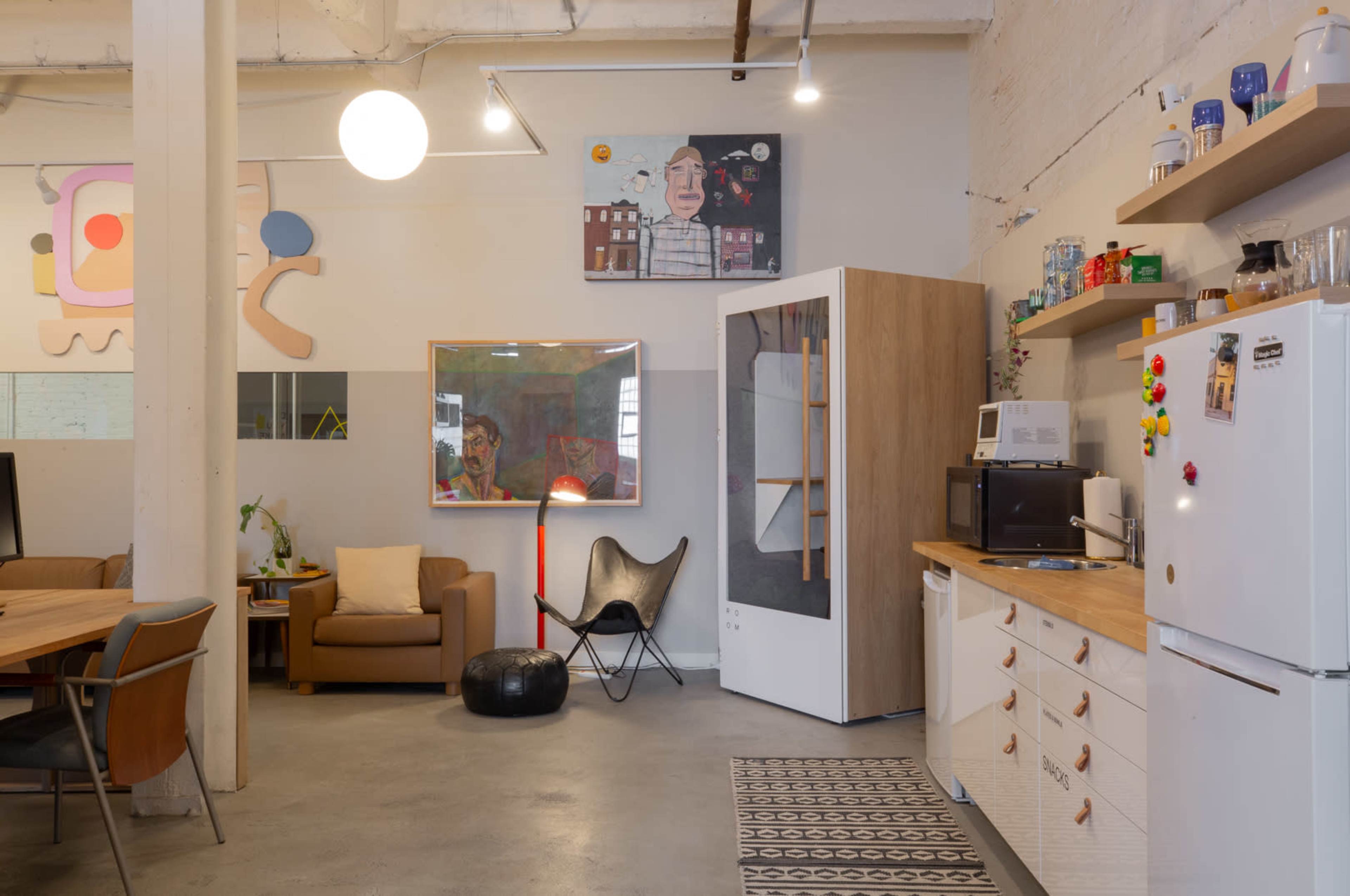 A modern kitchen and living area with a table, chairs, and various appliances, framed artwork, and a mix of colorful decorations.