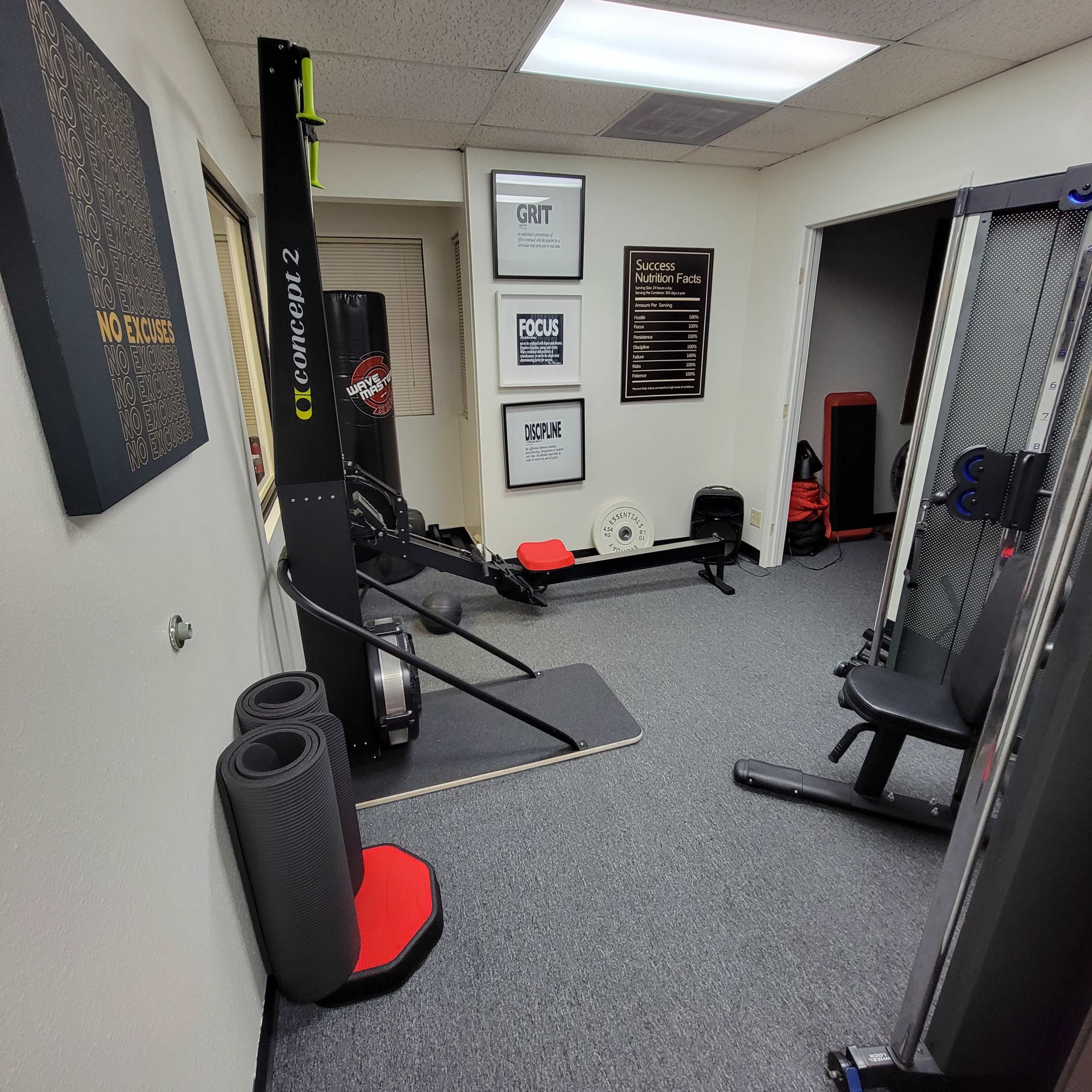 A small home gym featuring a rowing machine, a weight bench, exercise mats, and motivational posters on the walls.