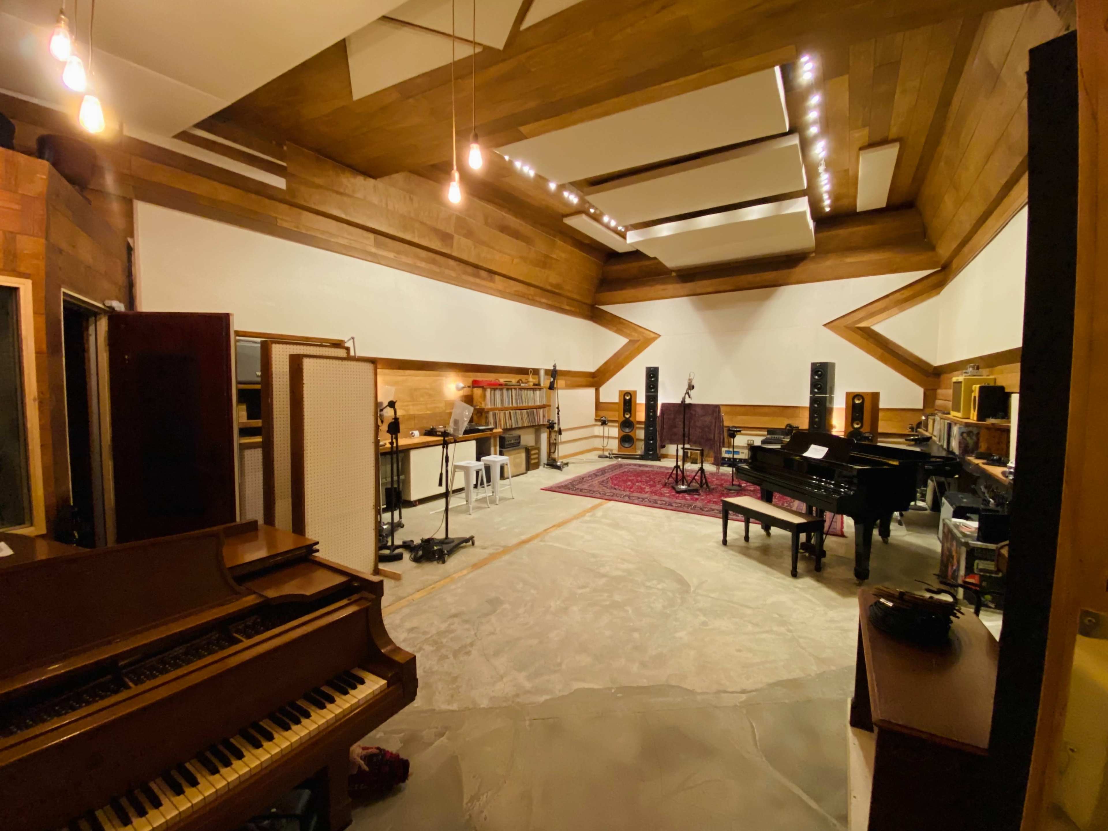 A spacious music recording studio featuring a grand piano, audio equipment, and wooden paneled walls.