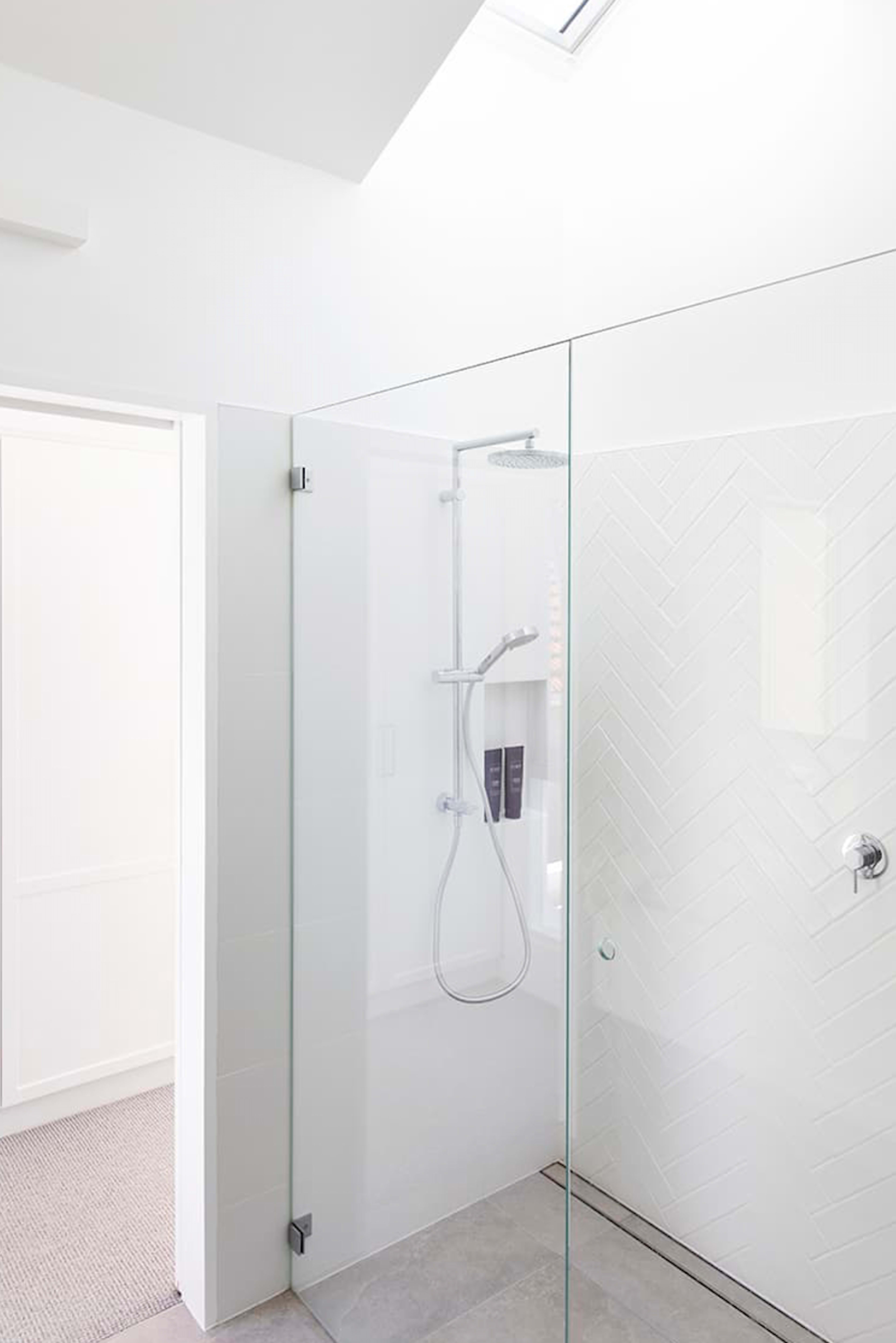 A modern glass-enclosed shower featuring a rainfall showerhead and a tiled wall with a herringbone pattern.