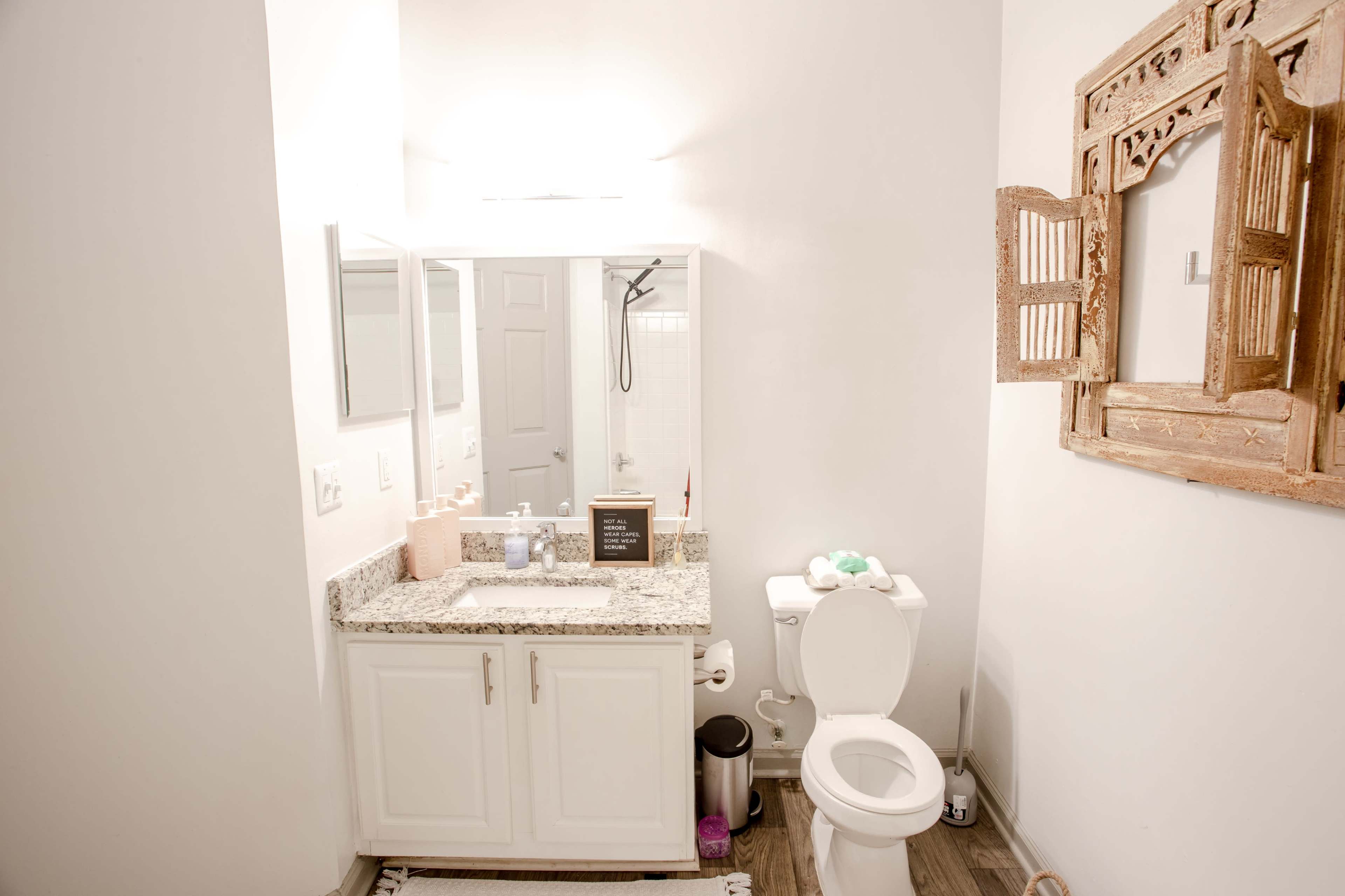 A small bathroom featuring a granite countertop with a sink, a toilet, and a wooden decorative mirror on the wall.