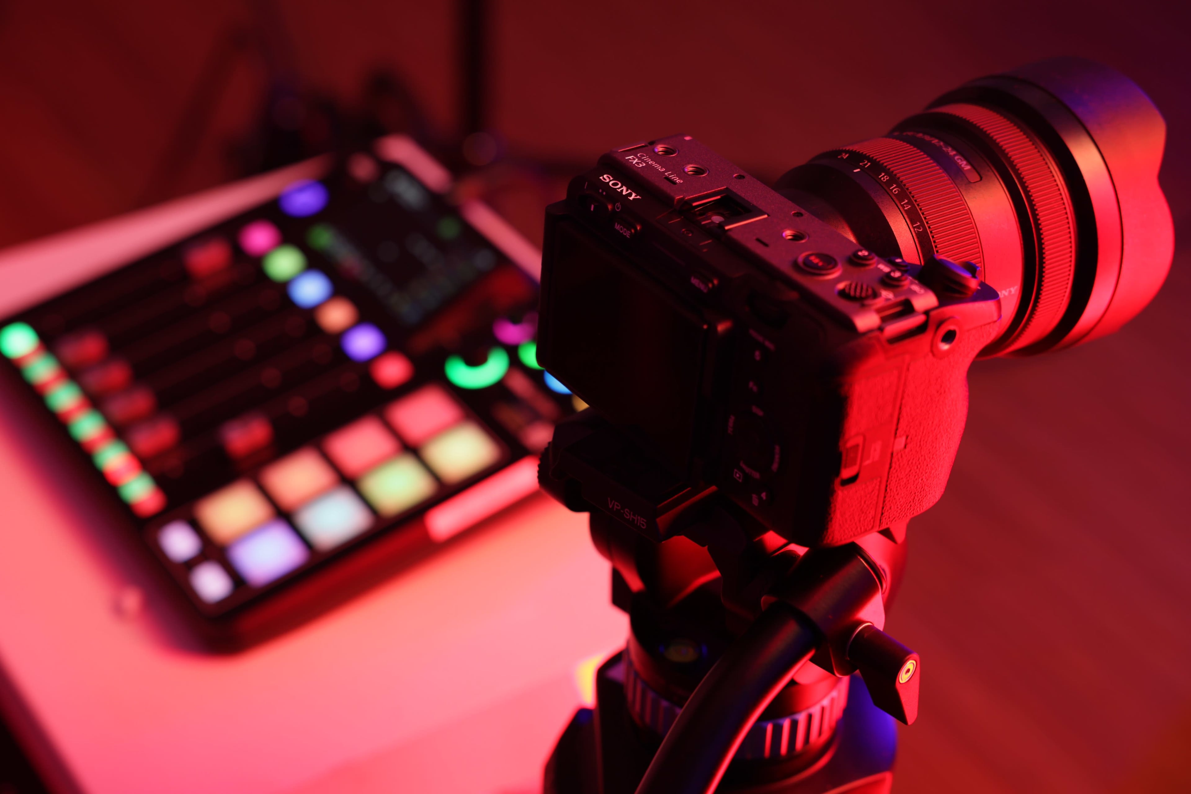 A camera is positioned on a tripod, focusing on a colorful control interface with illuminated buttons.