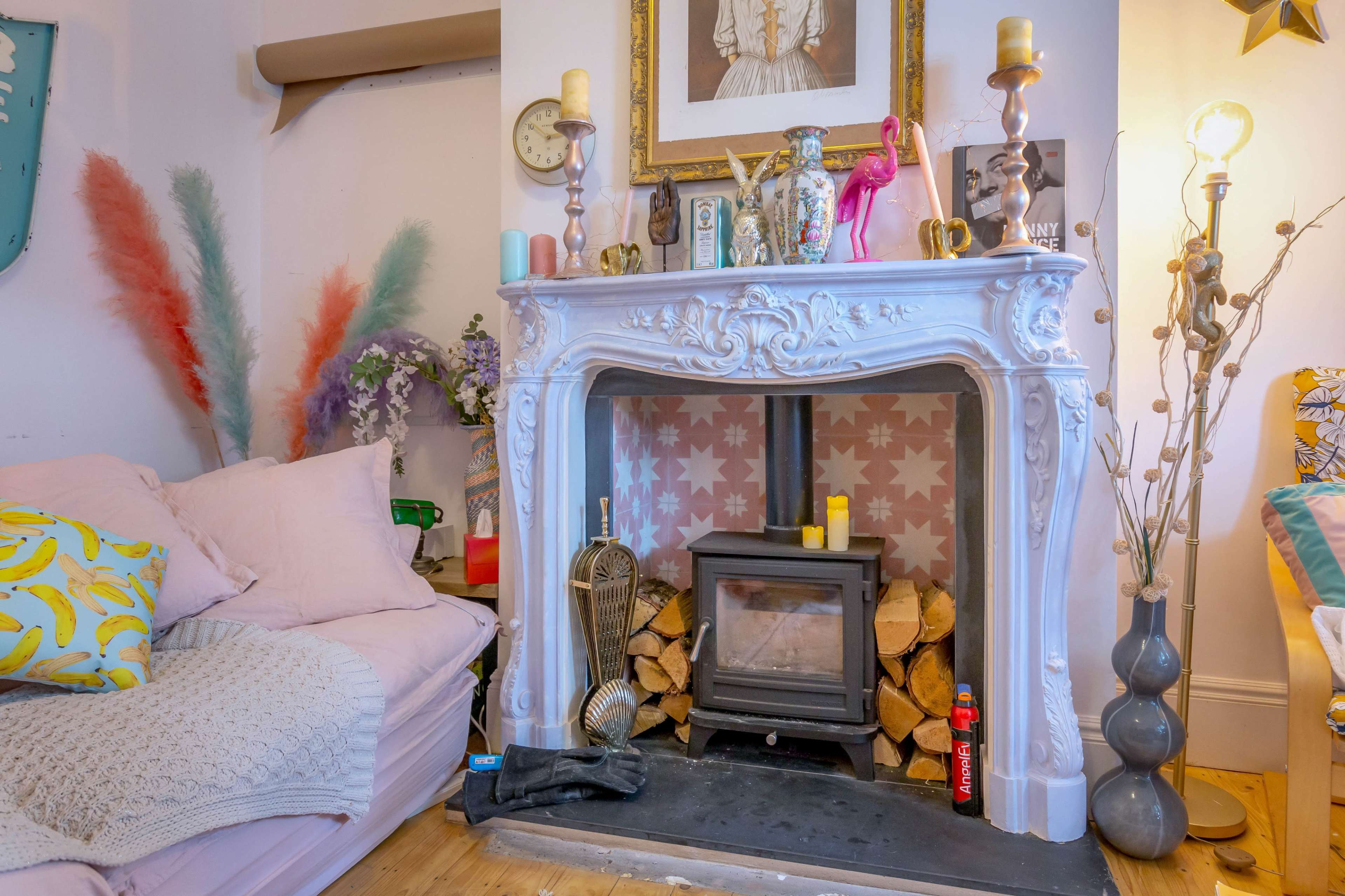 A cozy living room featuring a decorative white fireplace with a modern wood stove, surrounded by colorful decor and plants.