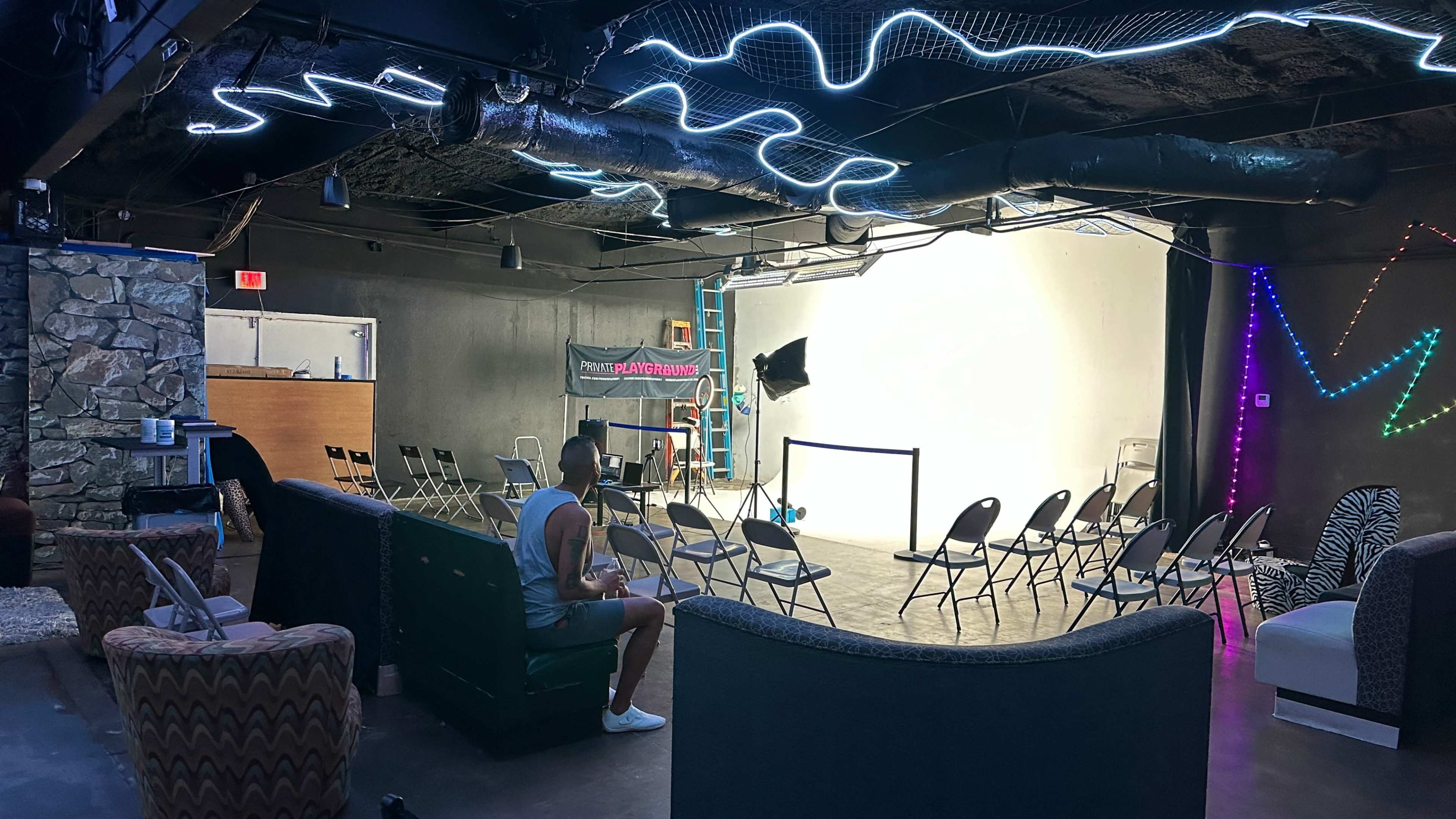 An empty room with chairs arranged in rows facing a blank wall, illuminated by colorful neon lights.