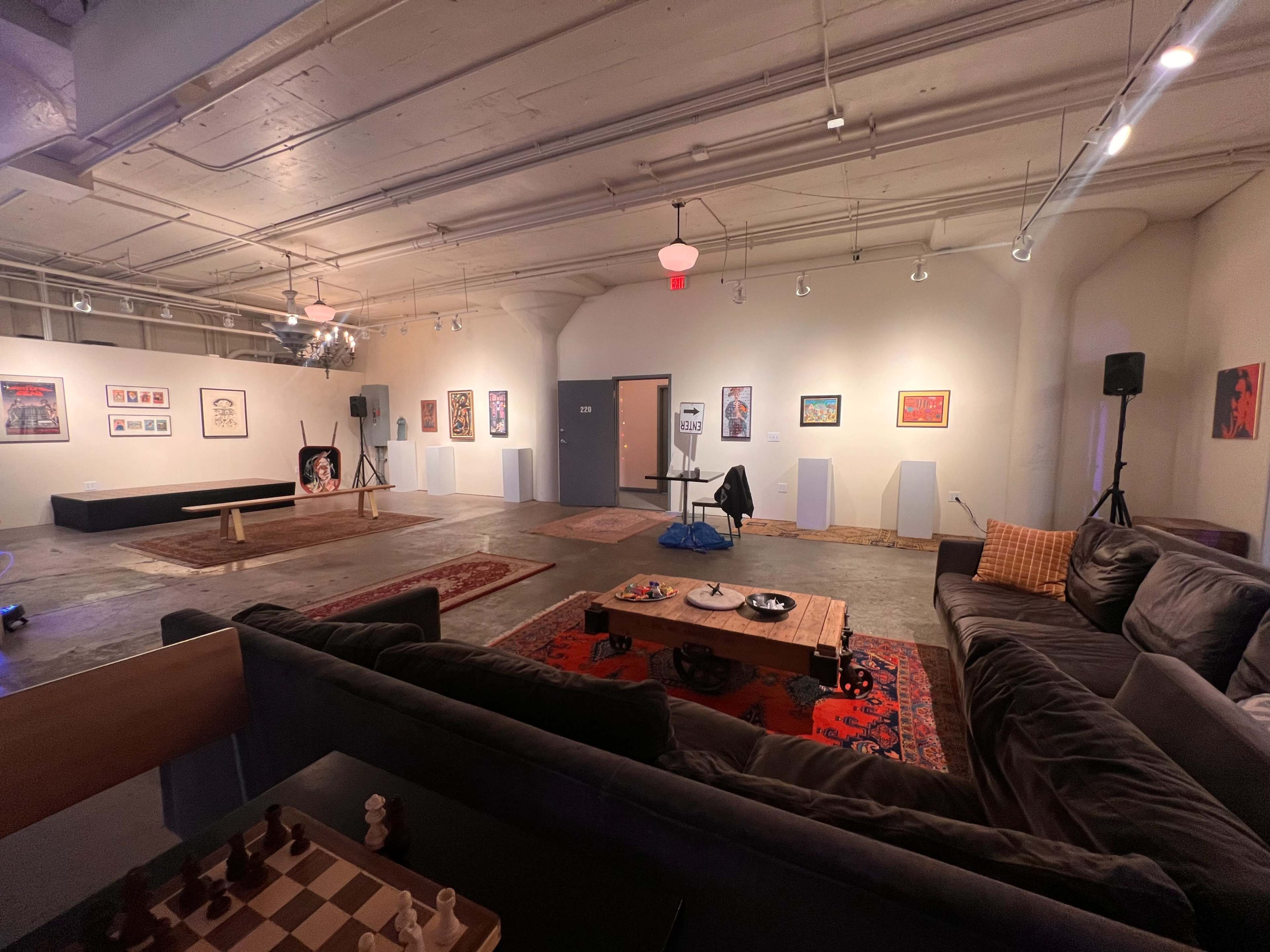 A spacious gallery or lounge area with a mixture of seating, artwork on the walls, and a chessboard in the foreground.