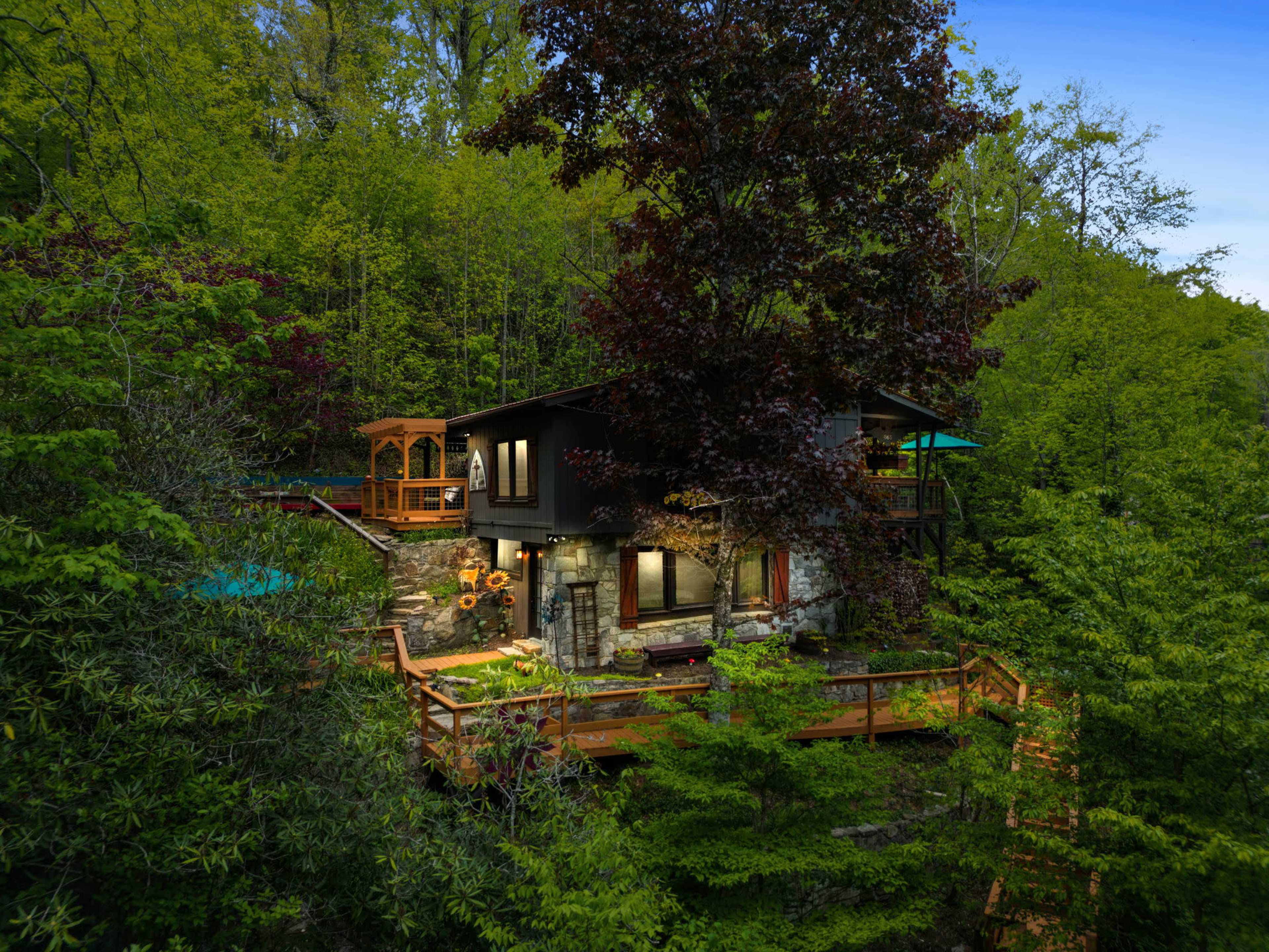 A modern house surrounded by dense greenery, featuring wooden decks and a gazebo.
