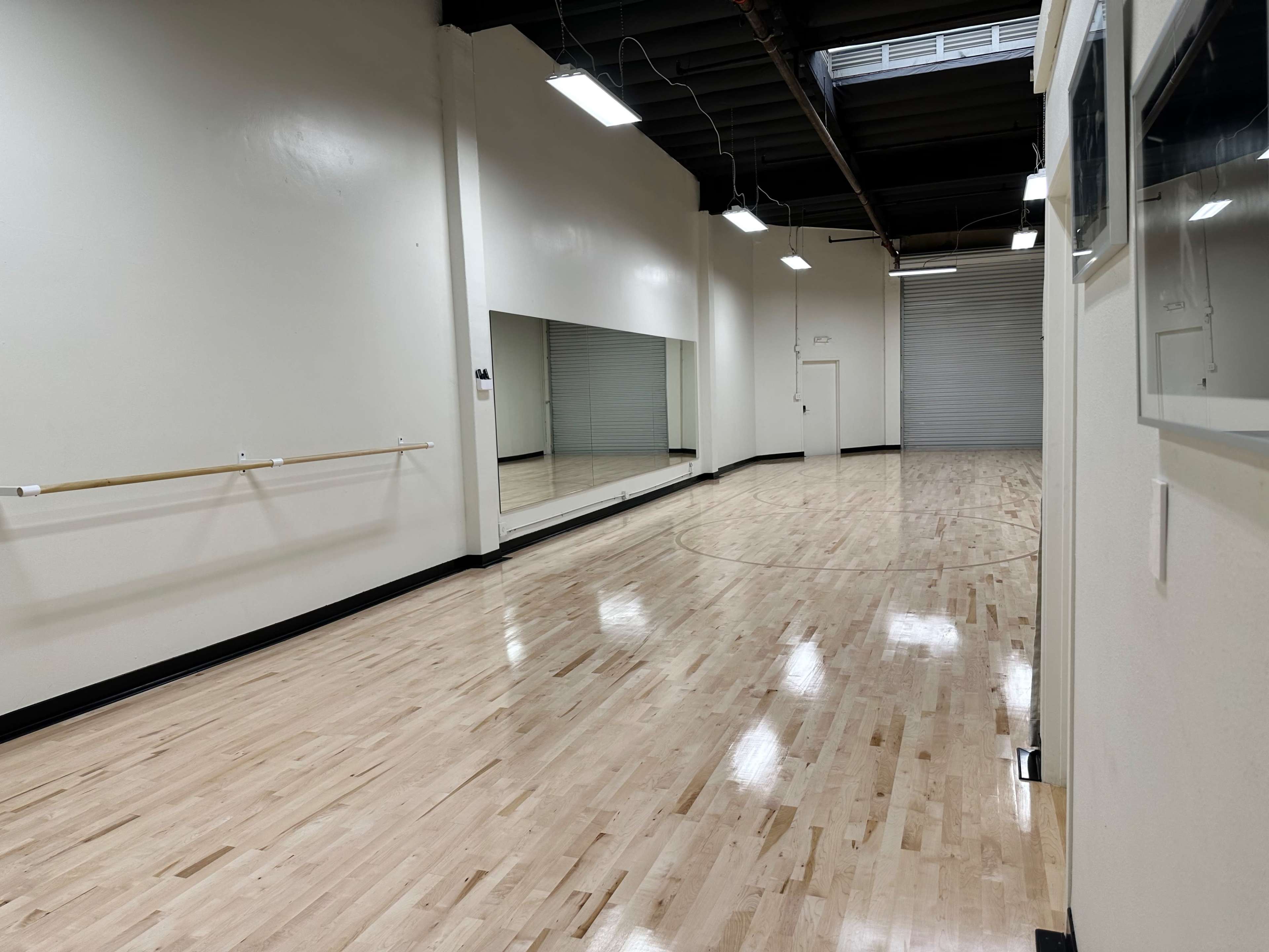A dance studio with a polished wooden floor, mirrors on one wall, and a barre along the opposite wall.
