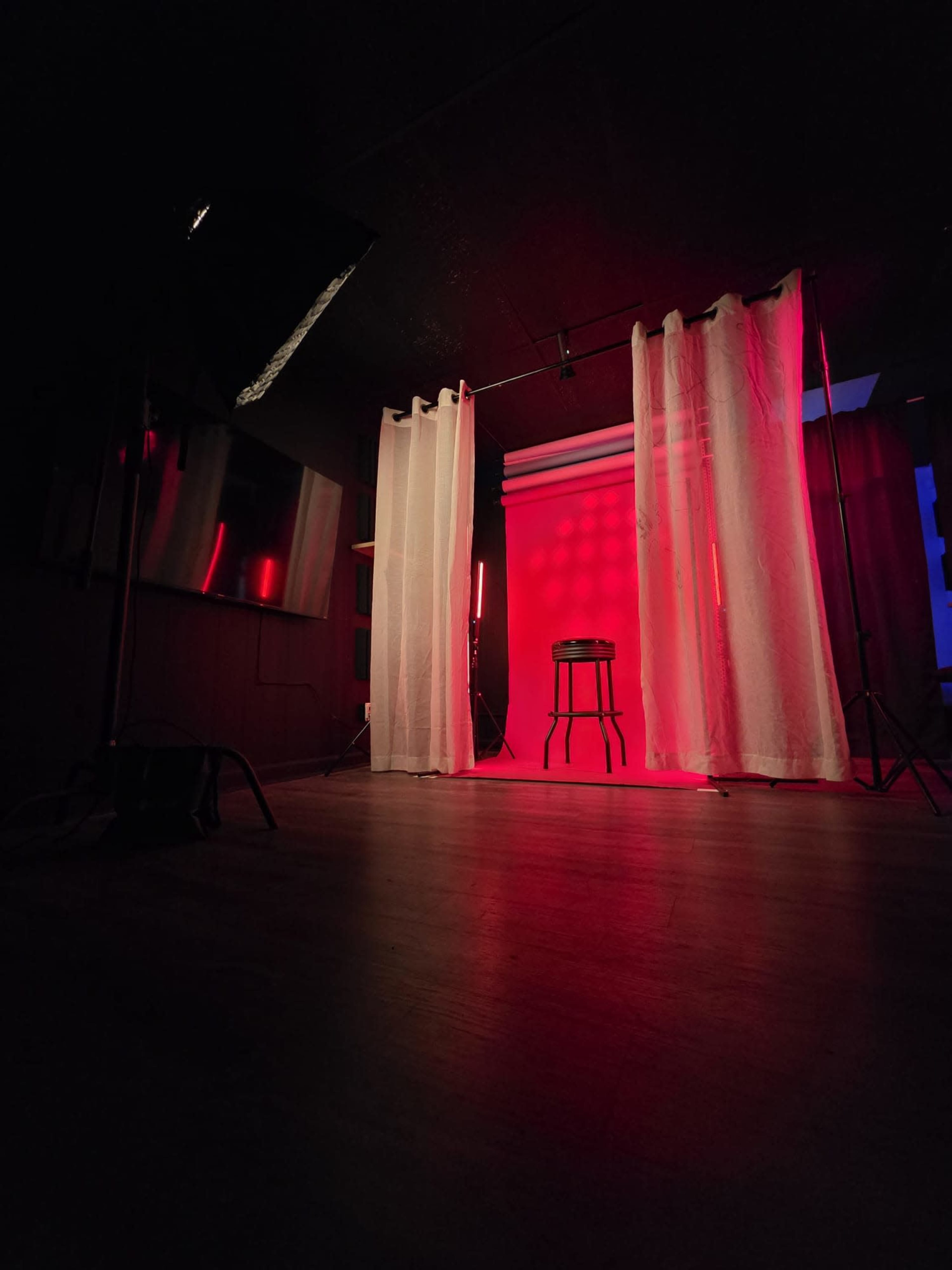 A photography studio features a stool positioned against a backdrop illuminated by red light, surrounded by sheer white curtains.