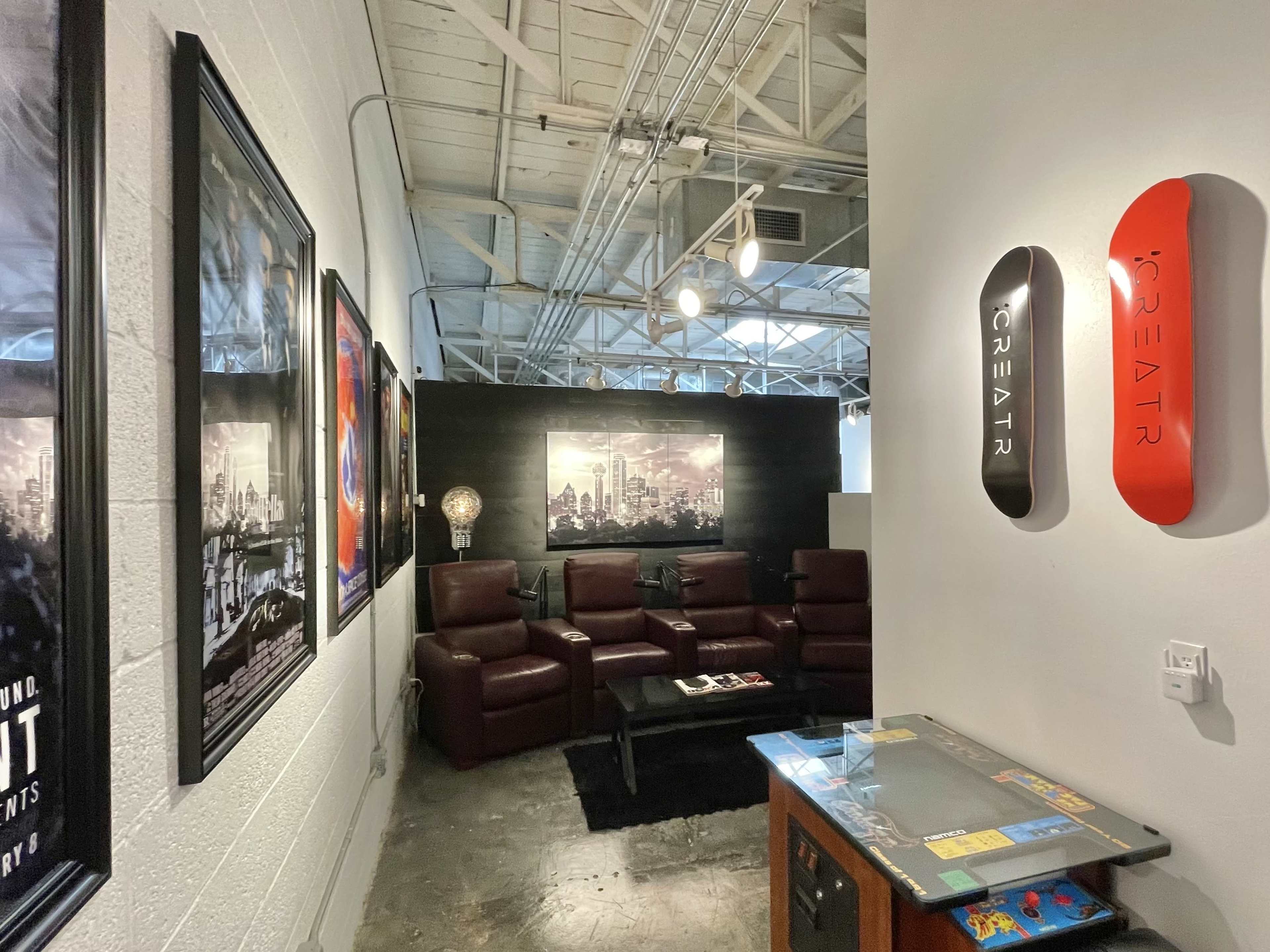 A modern lounge area with red leather chairs, framed movie posters on the walls, and a vintage arcade game table.