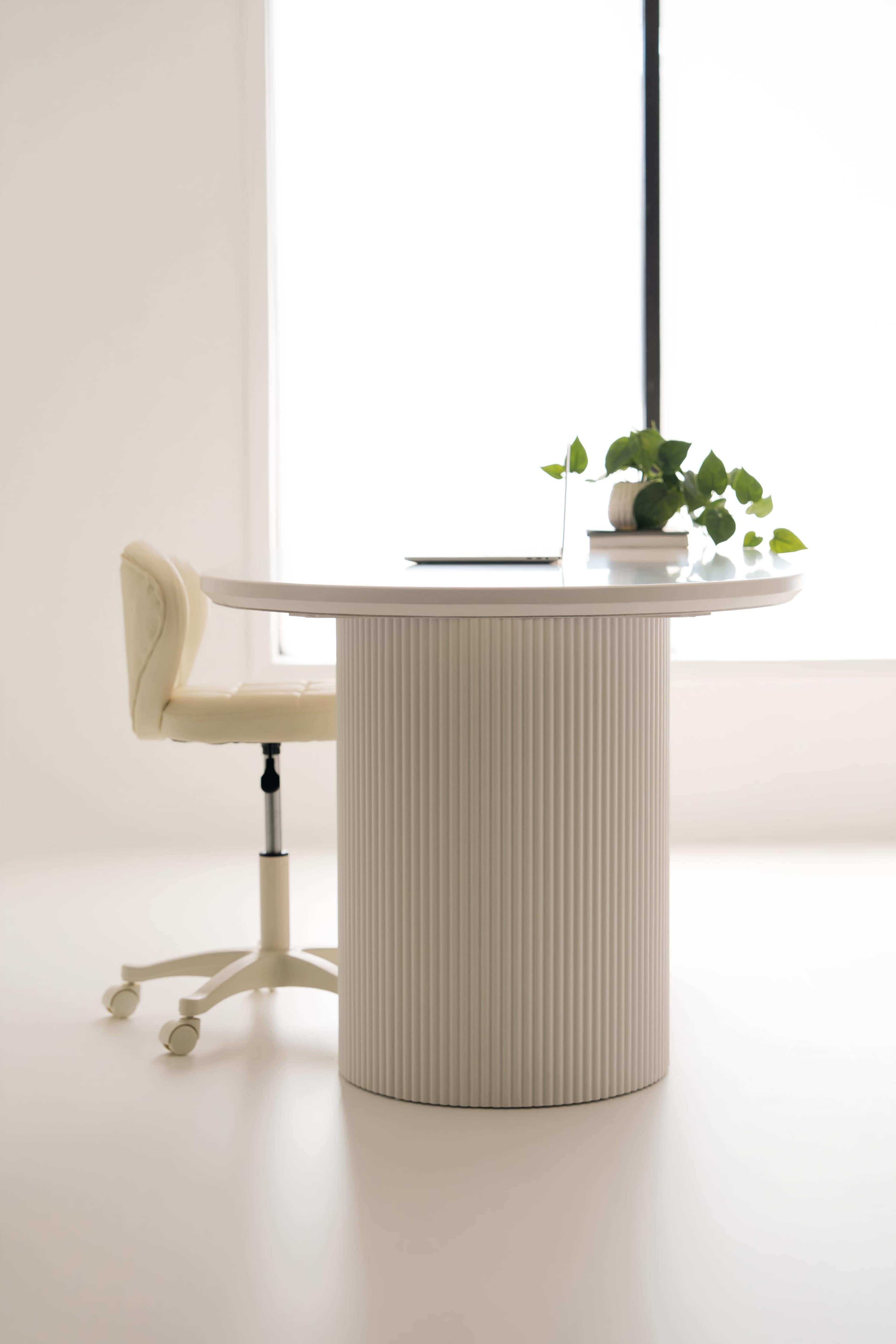 A round, ribbed table with a potted plant sits beside an office chair in a well-lit room.