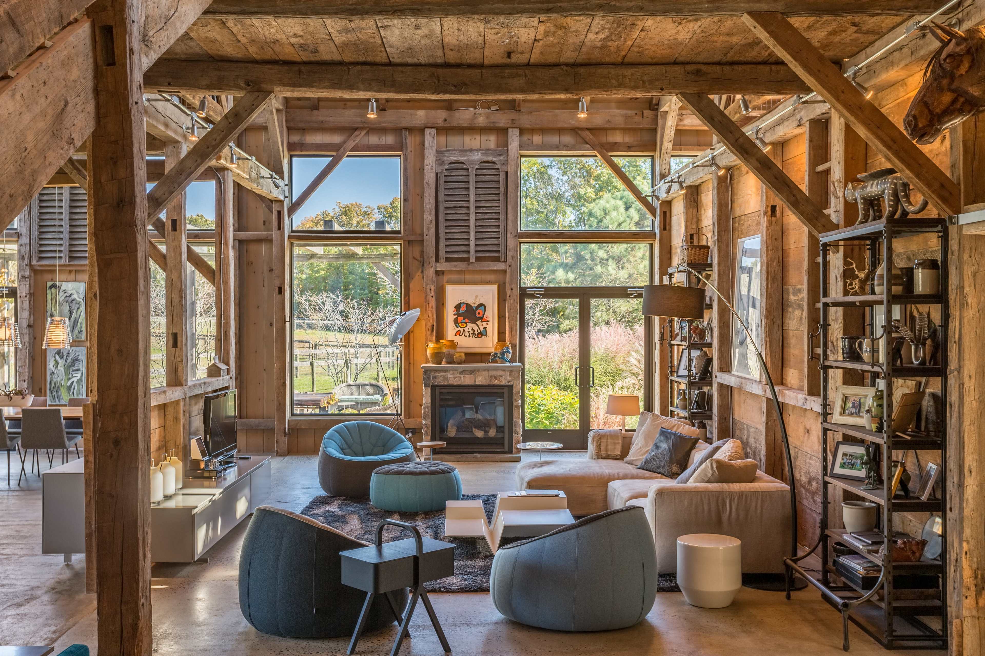 A spacious, rustic living room with exposed wooden beams, large windows, and a mix of modern and comfortable furniture arrangements.