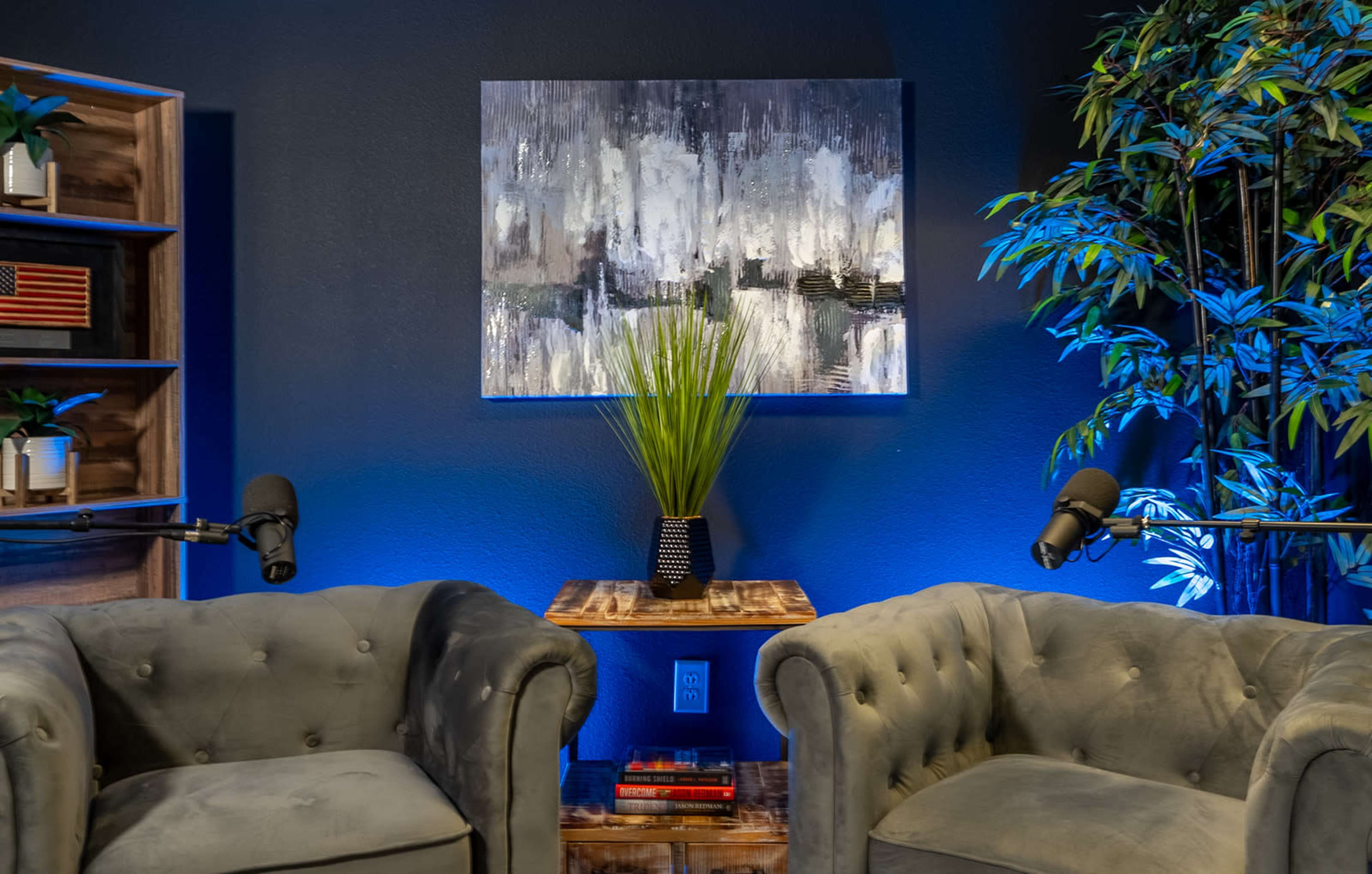 A modern conversation space features two upholstered chairs flanking a wooden side table with a vase of greenery, against a backdrop of abstract art.