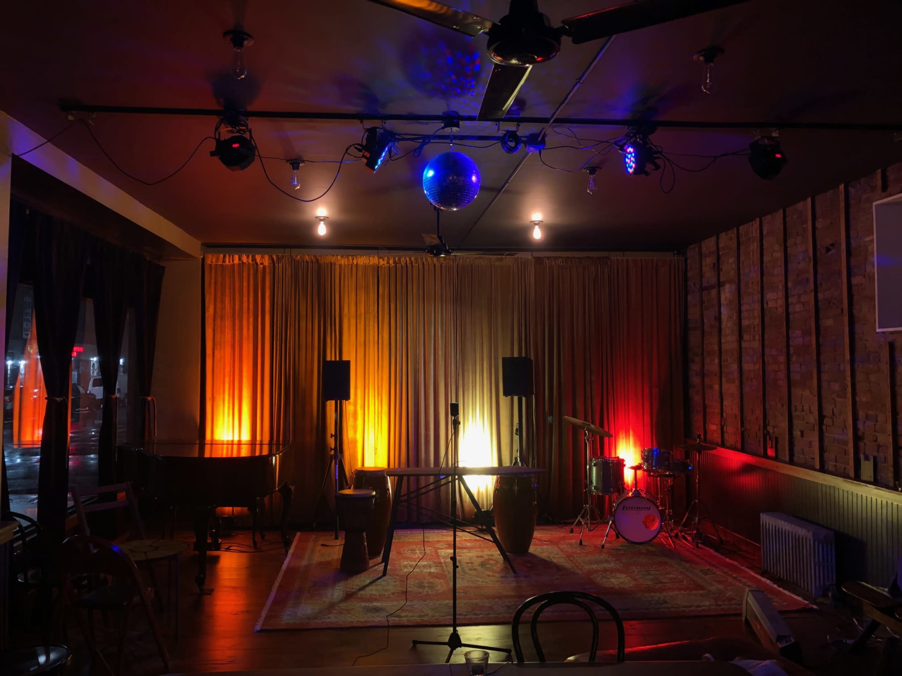 A dimly lit performance space with a stage, complete with a drum set and various lighting effects.