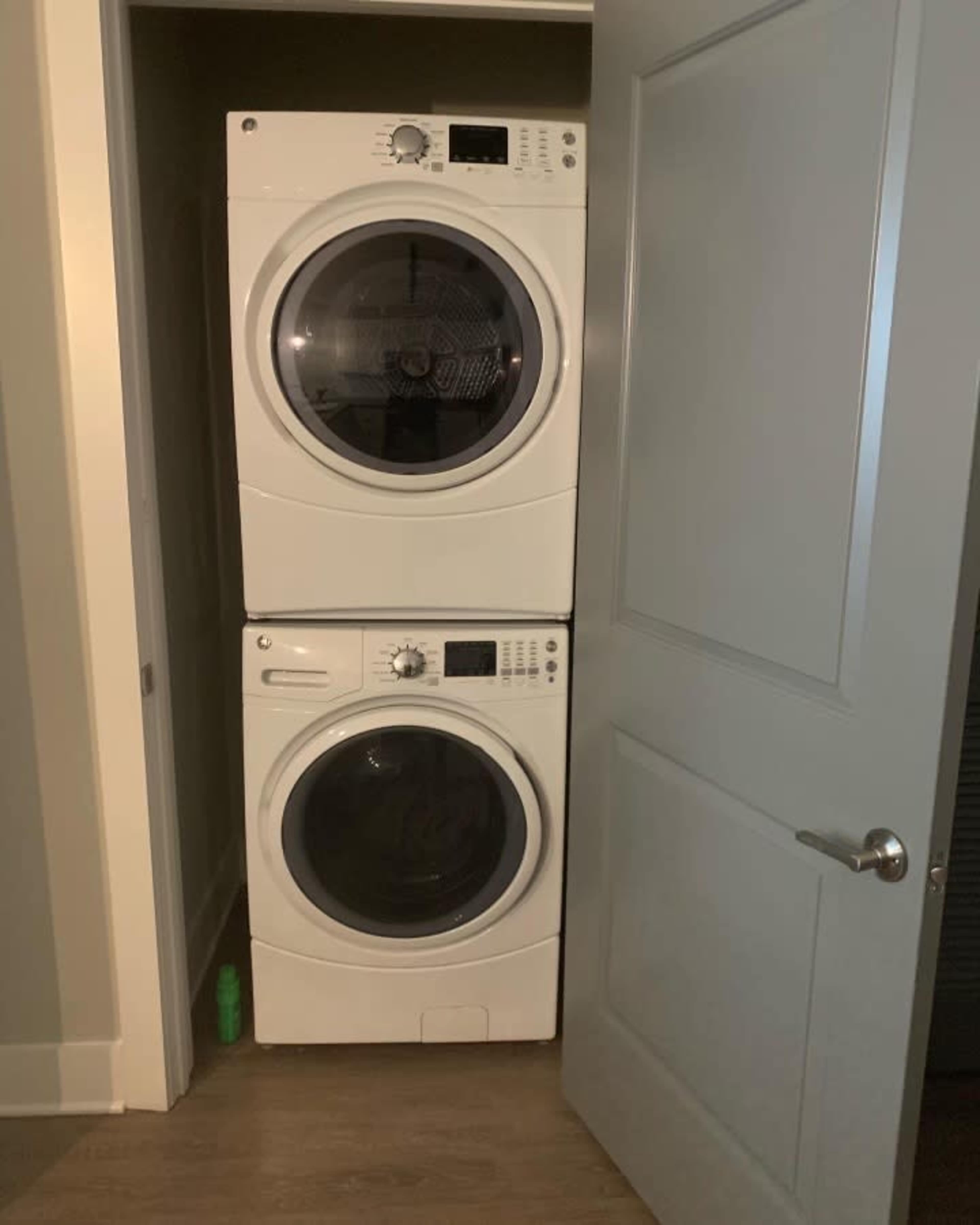 A stacked washer and dryer are positioned inside a small closet with a partially open door.