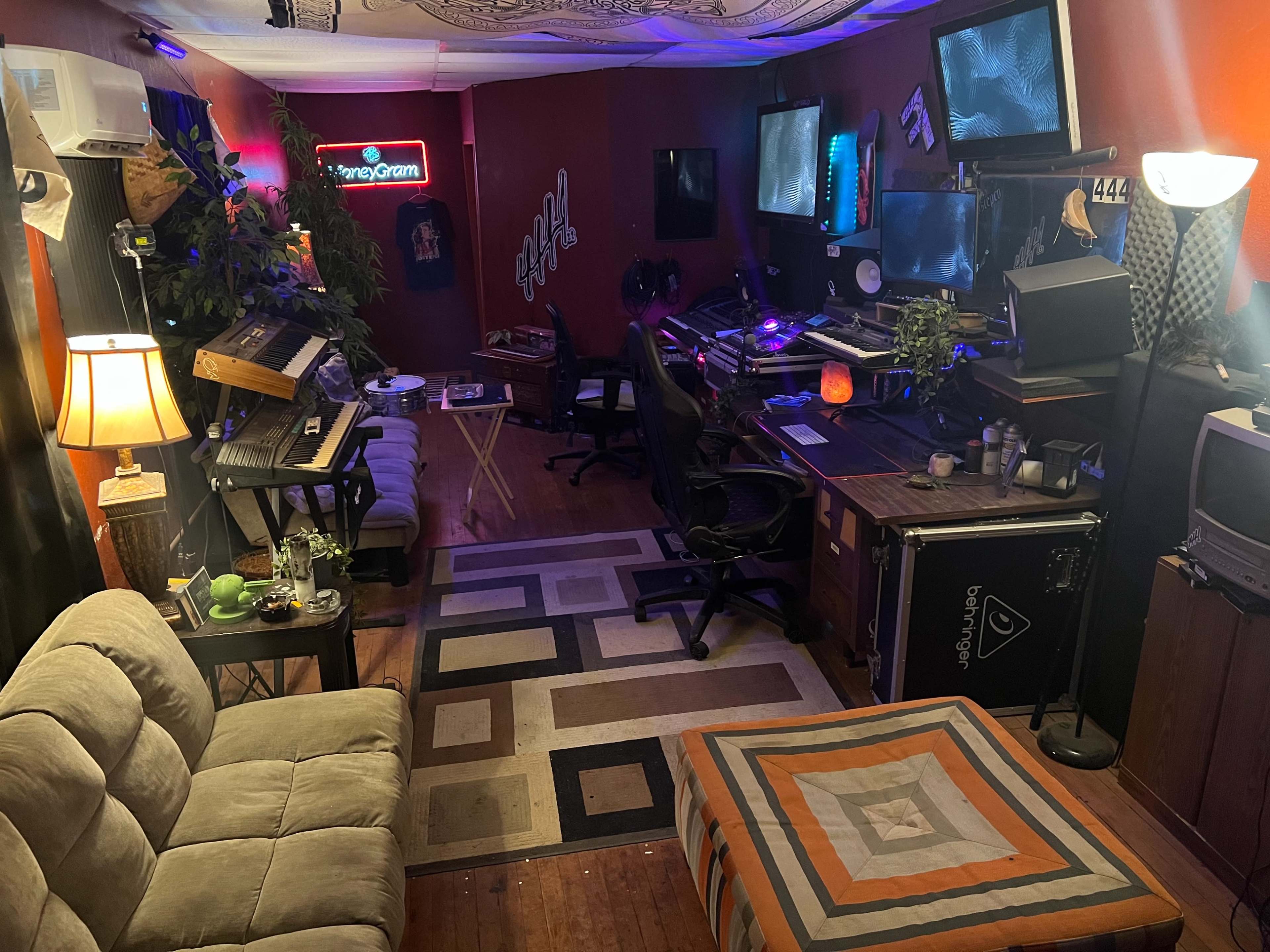 A cozy recording studio featuring various electronic equipment, a keyboard, monitors, and a seating area with a patterned rug.