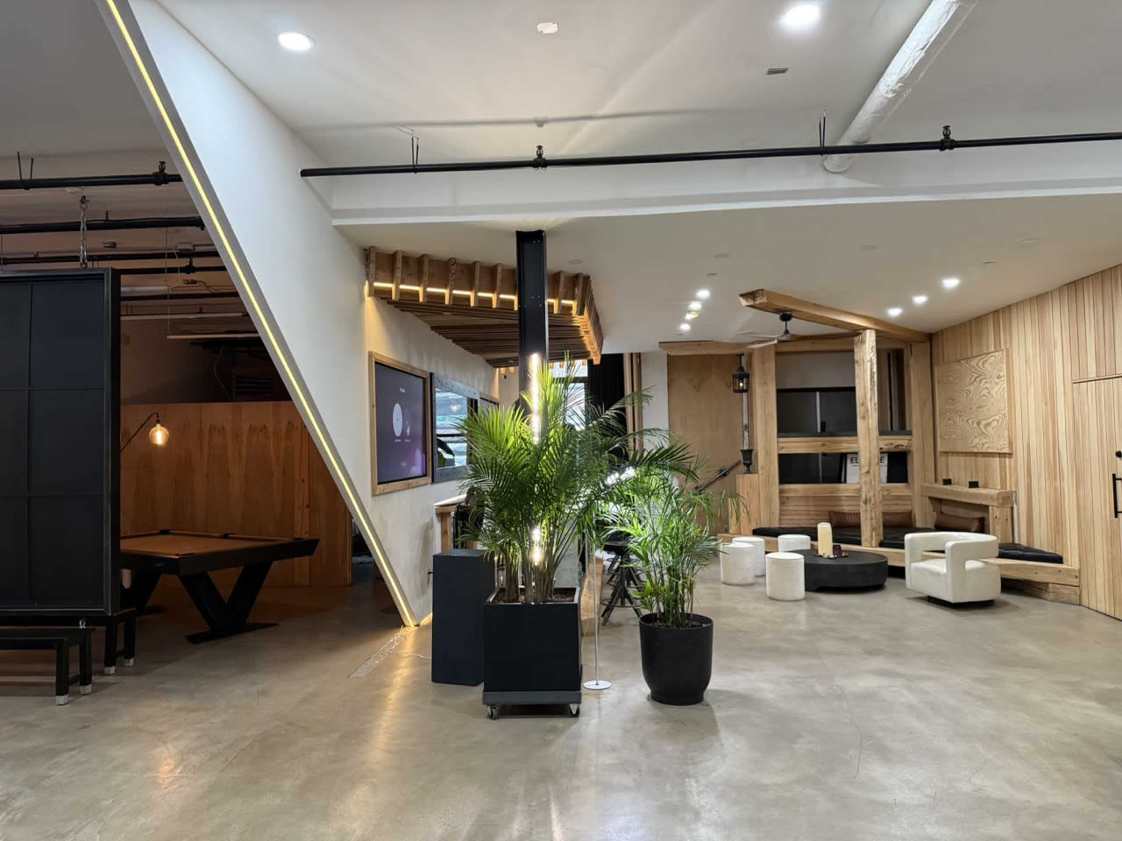 The image shows a modern interior space with a lounge area featuring wooden accents, seating arrangements, and indoor plants.