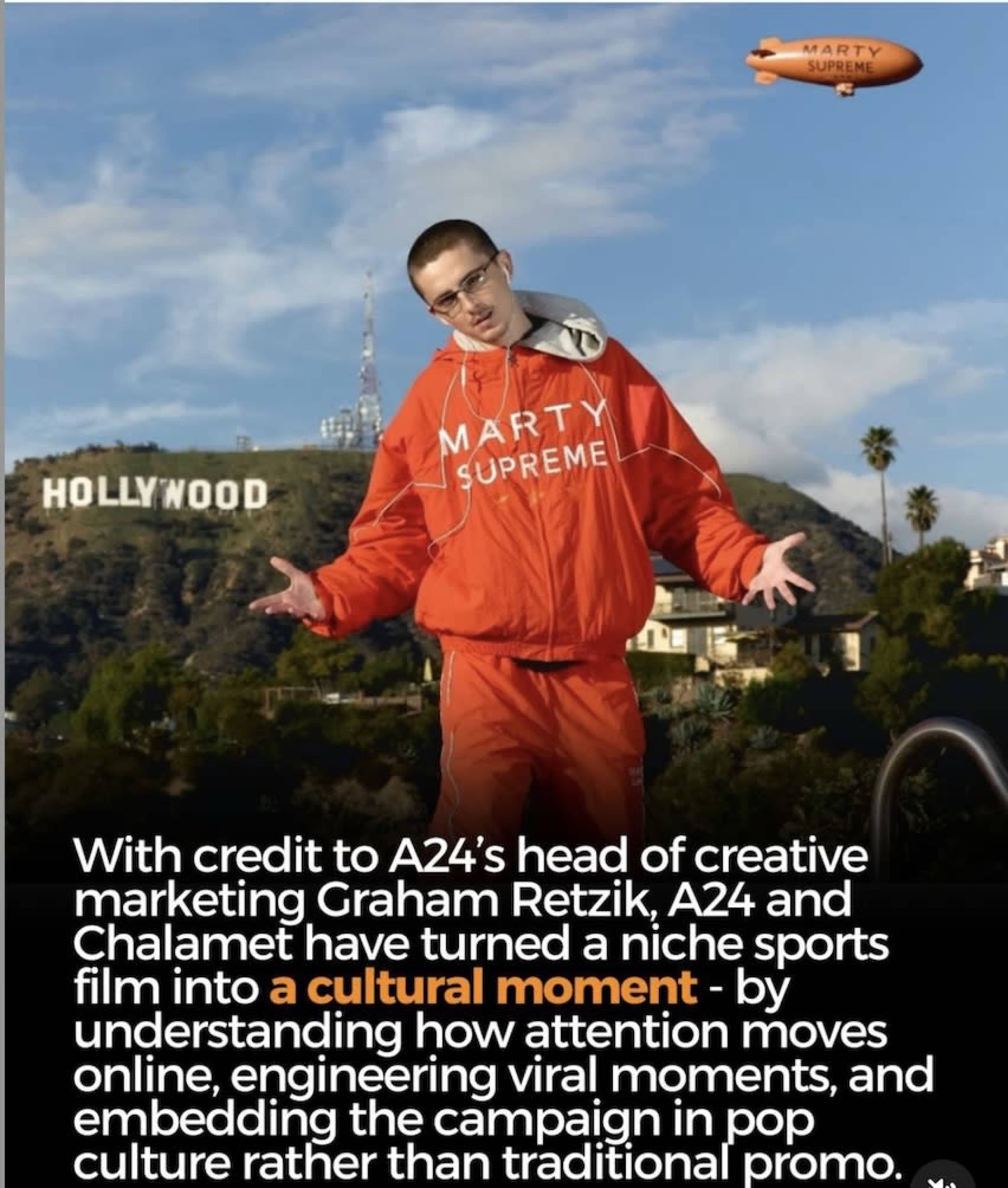 A man in an orange jumpsuit poses in front of the Hollywood sign while promoting a film related to cultural marketing.