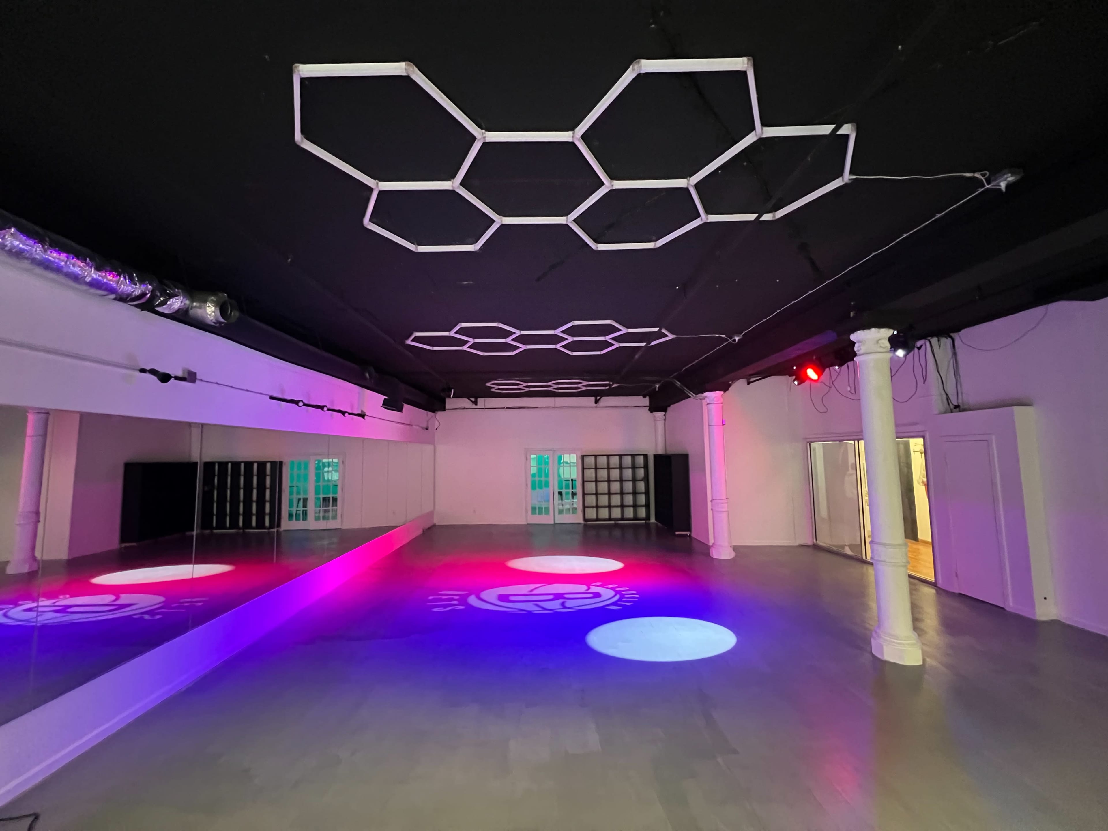 The image shows an empty dance studio with a mirrored wall, colorful lights, and geometric ceiling decorations.