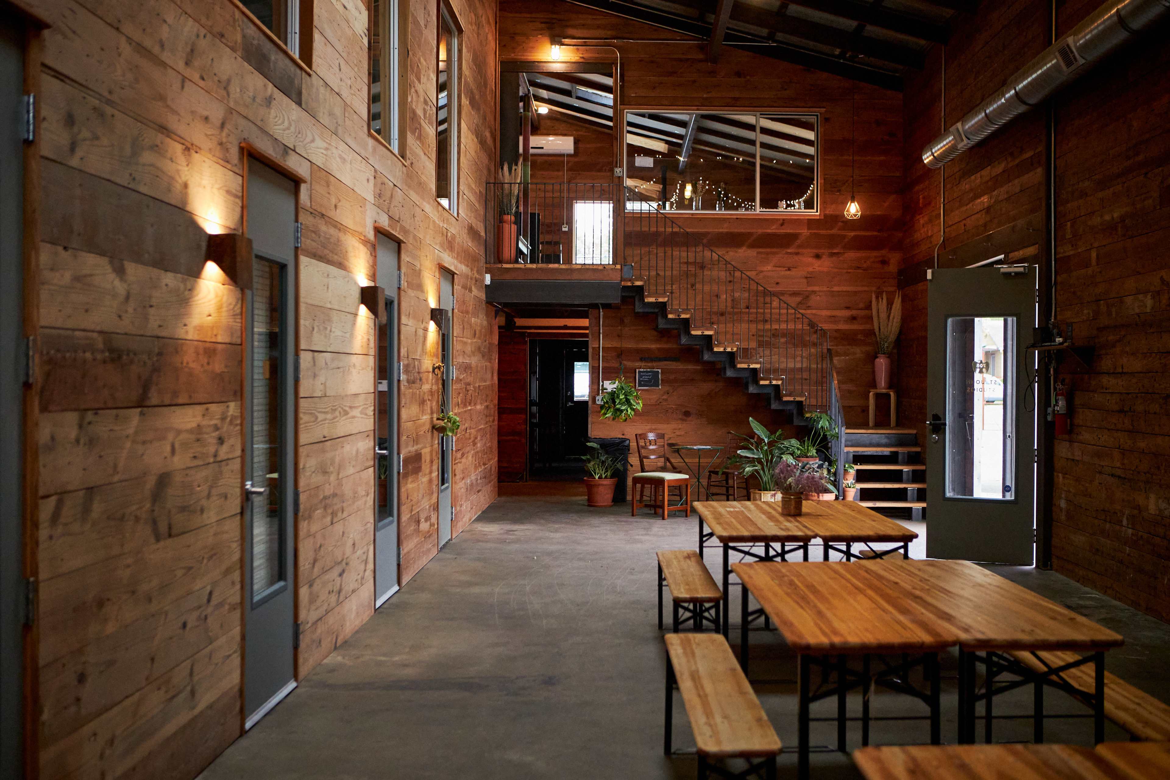 A spacious, wooden interior of a building with stairs leading to an upper level and several tables arranged in the foreground.