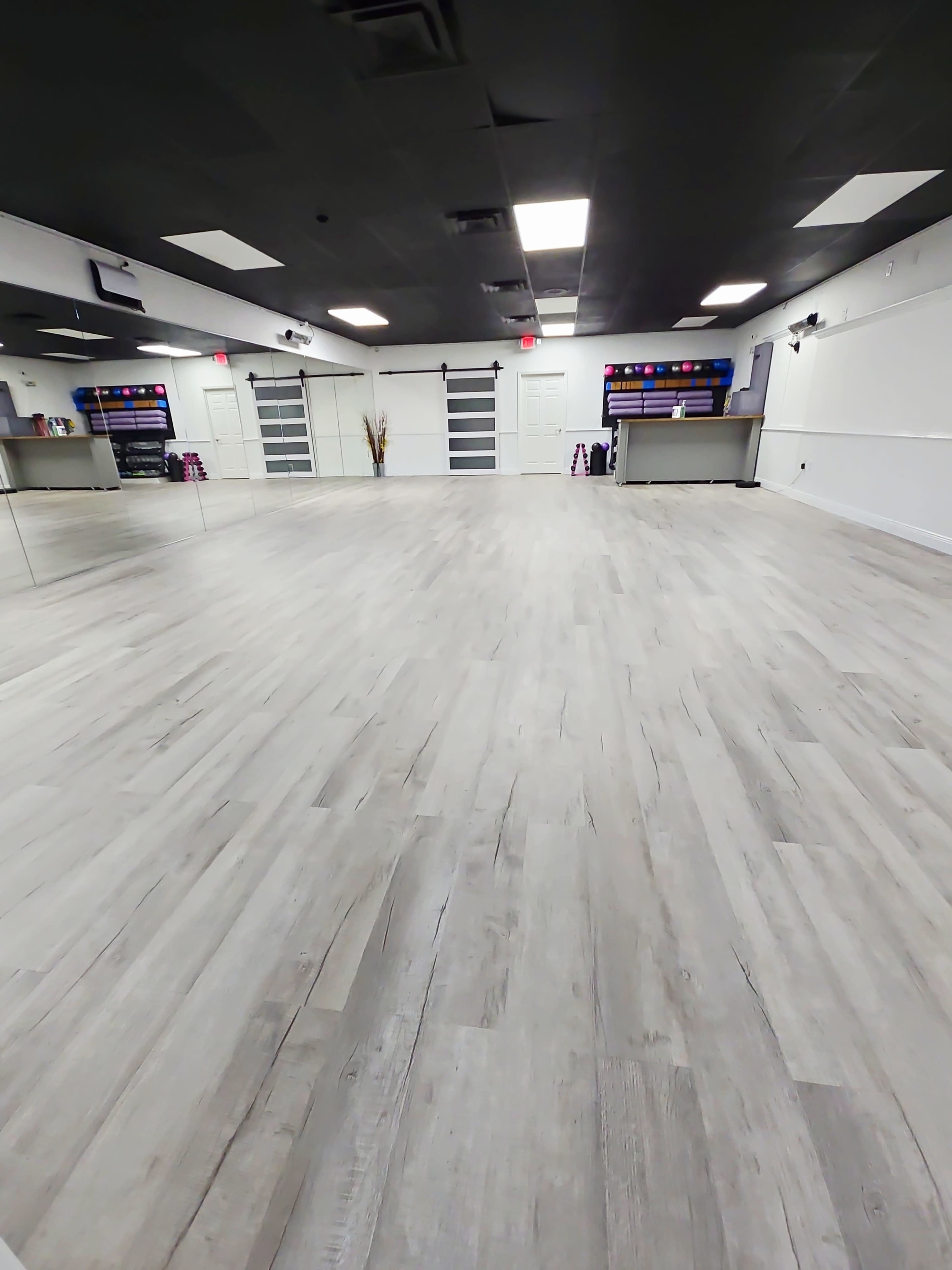 The image shows a spacious, empty dance studio with light-colored wooden flooring and large mirrors along one wall.