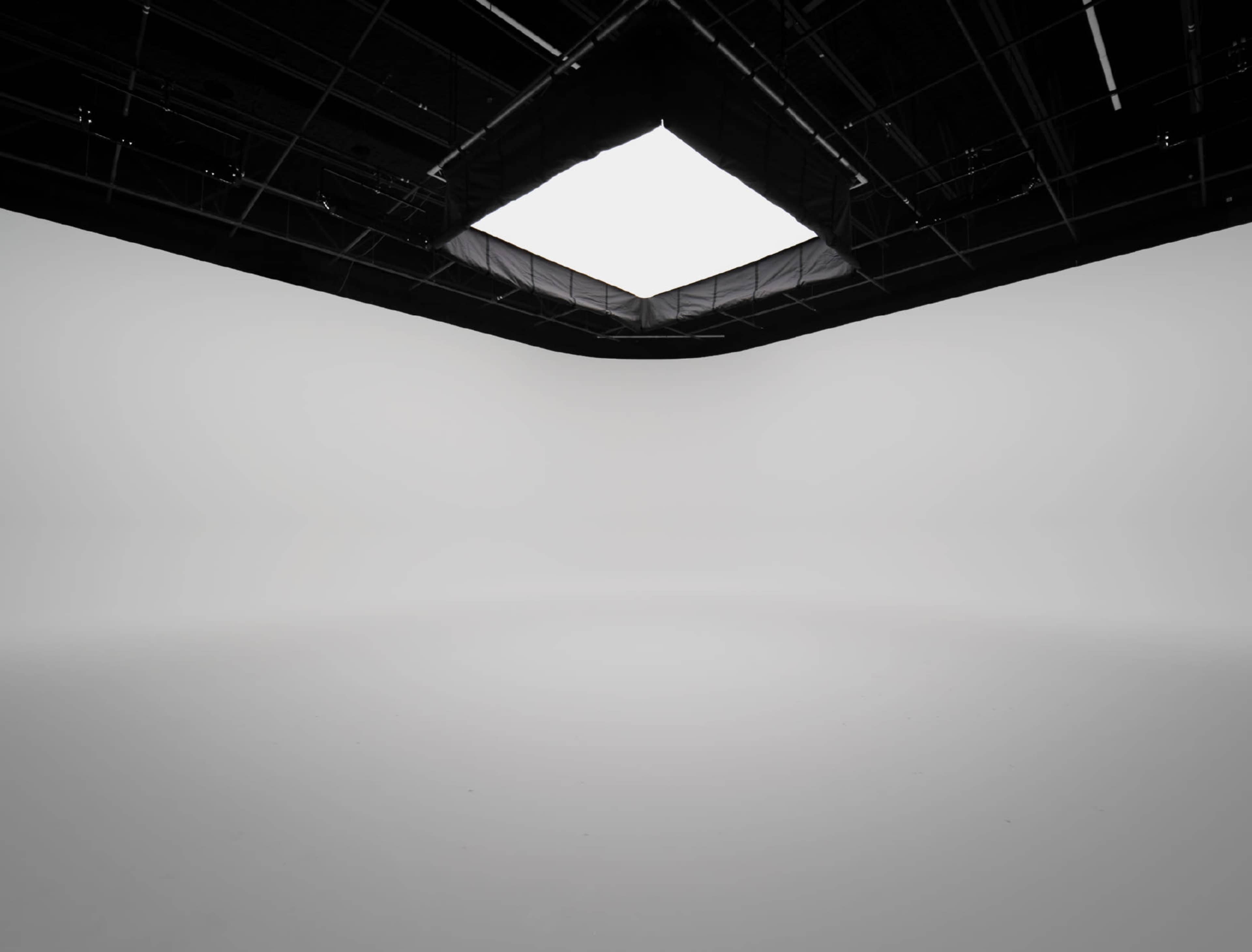 The image shows a minimalist studio space with a large square skylight above and plain white walls.