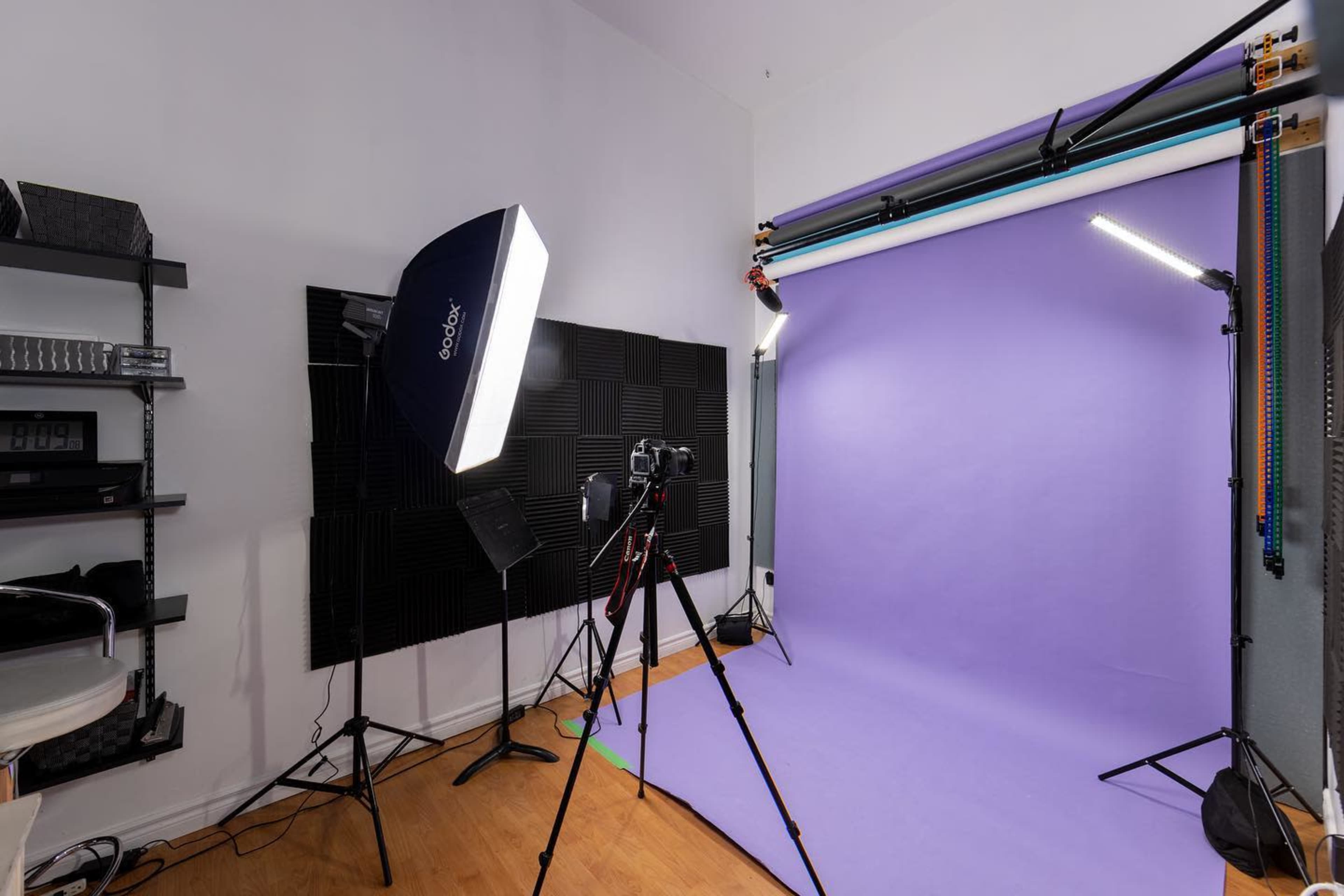 A photography studio with a purple backdrop, lighting equipment, and a camera set on a tripod.