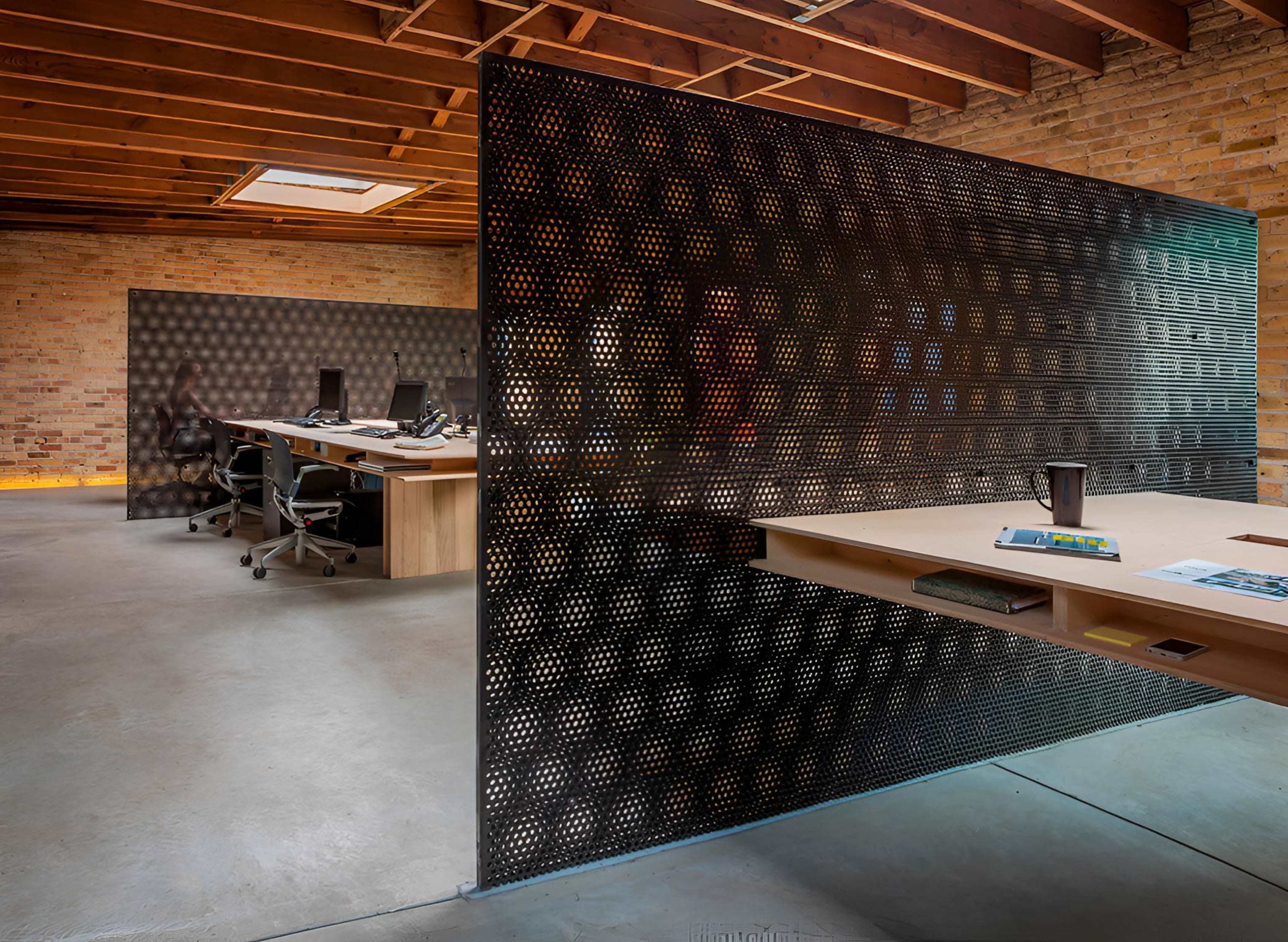 The image shows a modern office space featuring a perforated metal partition, two workstations with desks, and exposed wooden beams in the ceiling.