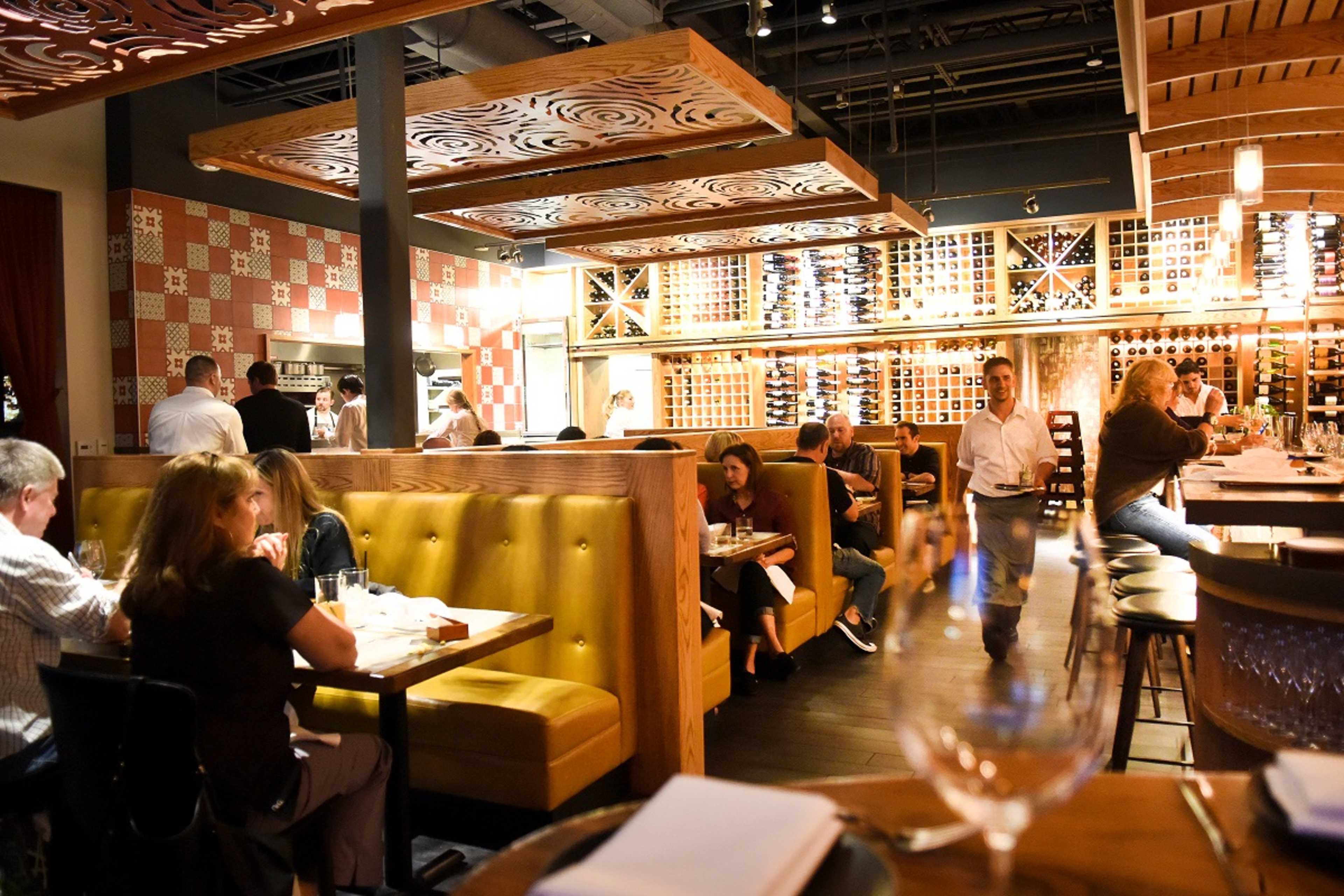 A modern restaurant interior with wooden booths, colorful wall decor, and patrons dining and interacting at tables.