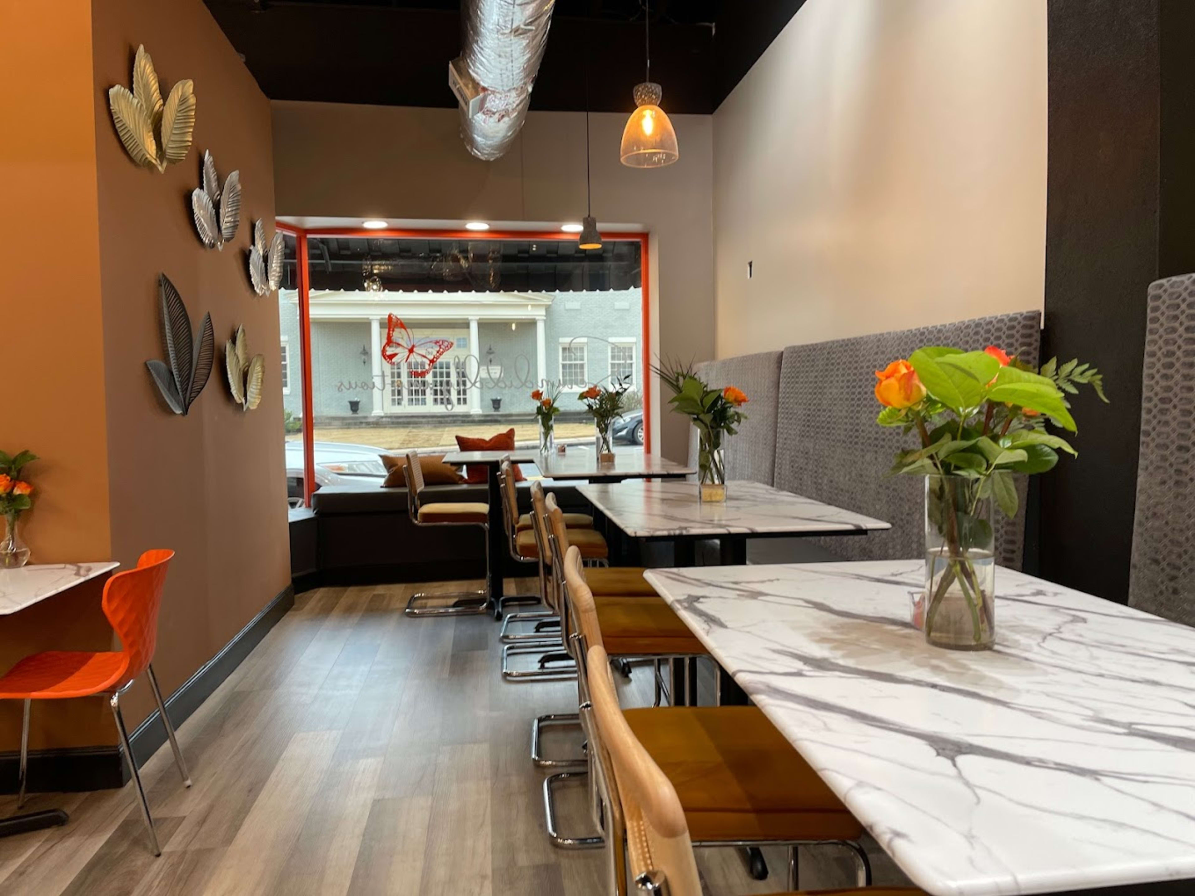 The image shows a modern café interior with marble tables, upholstered seating, and decorative wall art, illuminated by pendant lights.