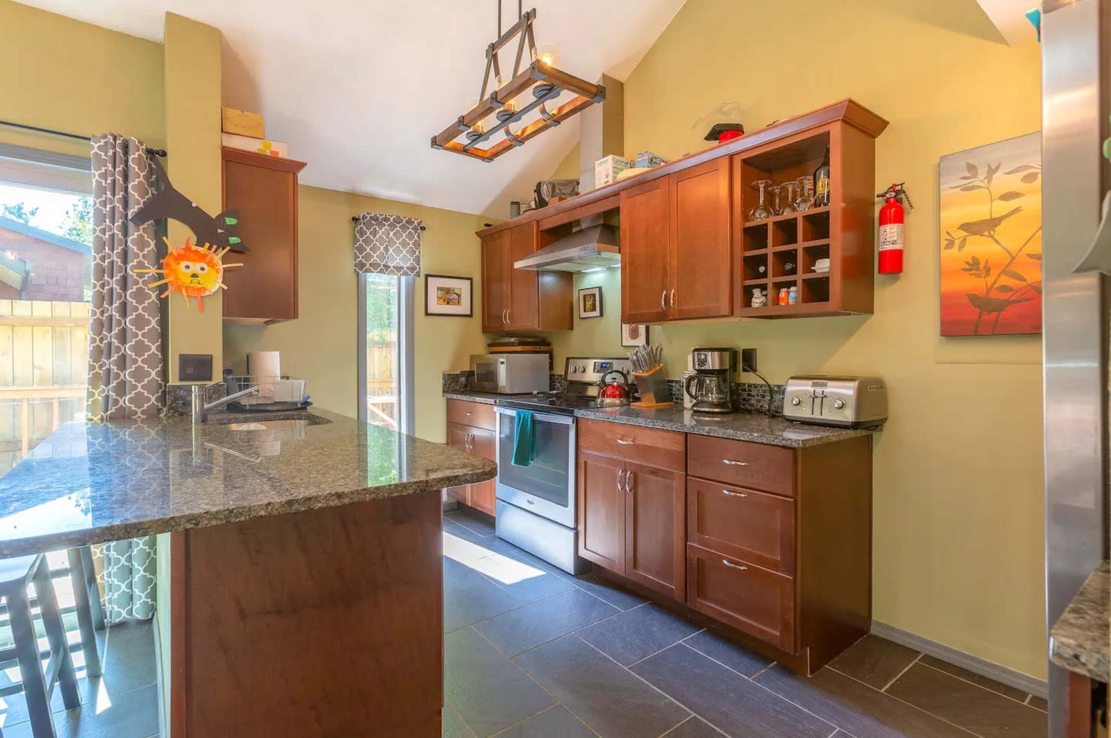 A modern kitchen with wooden cabinets, a granite countertop, and stainless steel appliances, featuring a view of an outdoor space through a sliding glass door.