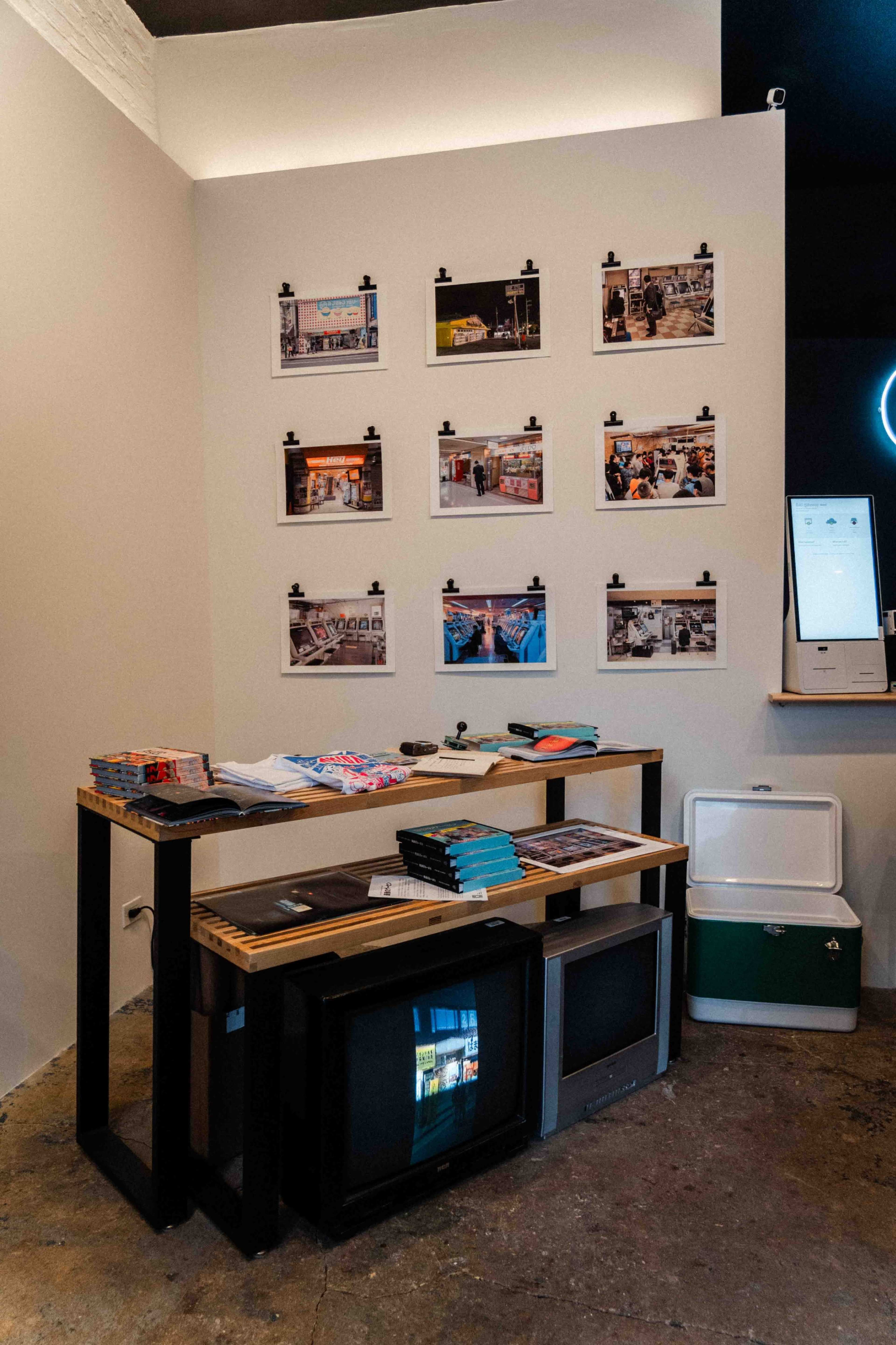 The image shows a corner of a store featuring a wall with framed photographs, a table with various brochures and magazines, and a vintage television set.