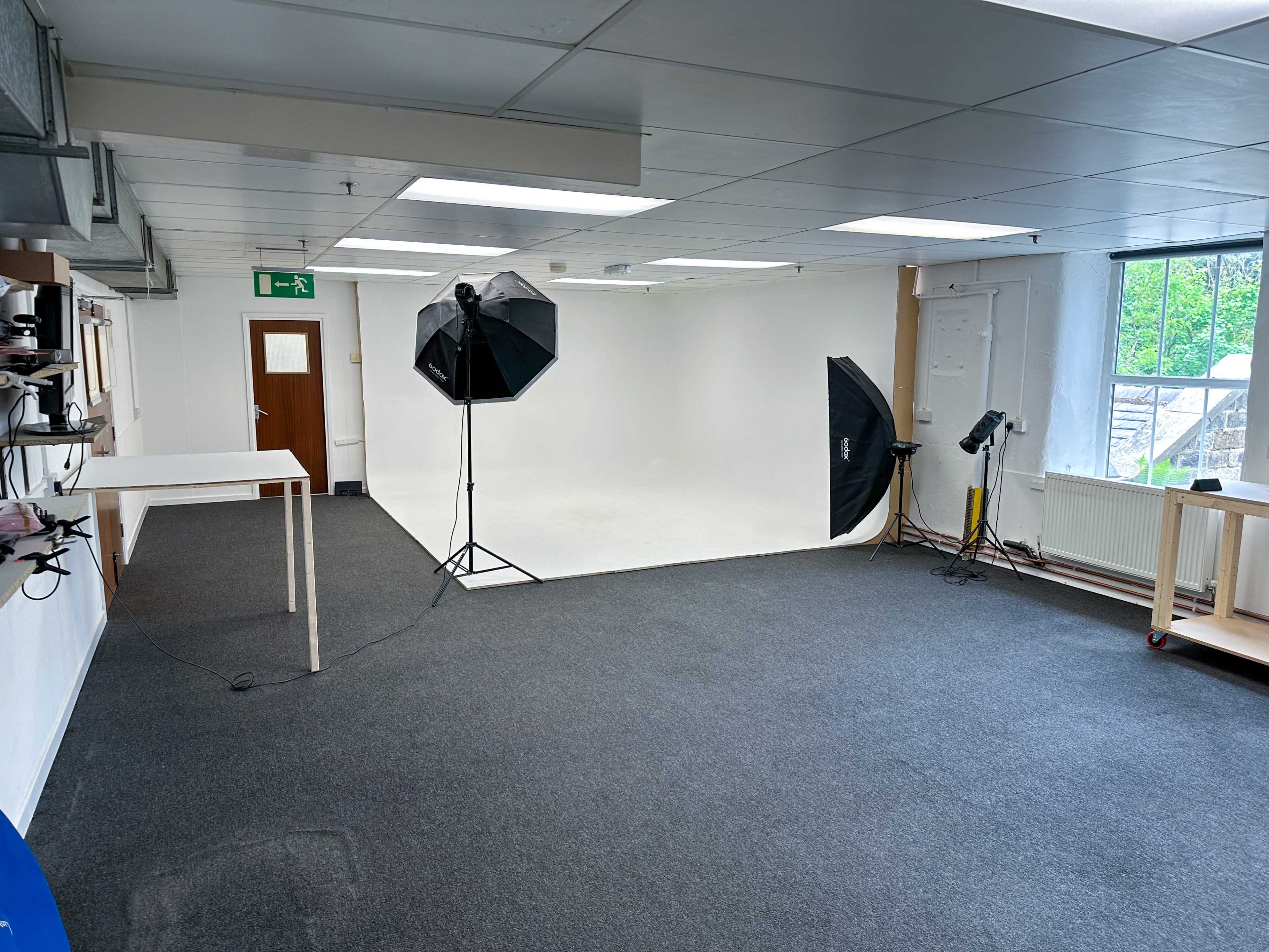A spacious, well-lit studio with a white backdrop and photography equipment set up in a plain room.