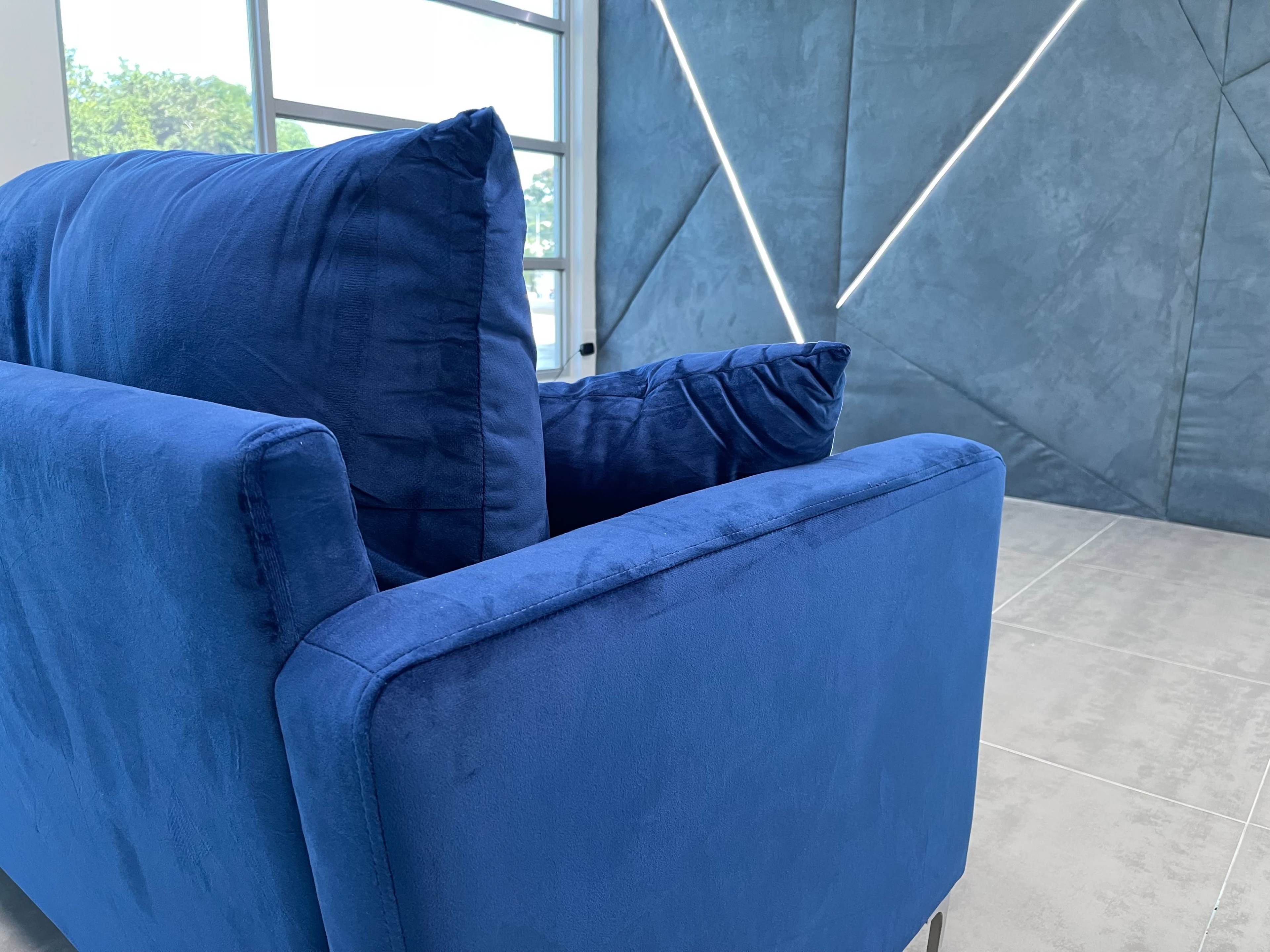 A blue fabric sofa is positioned in front of a textured wall with diagonal lighting.