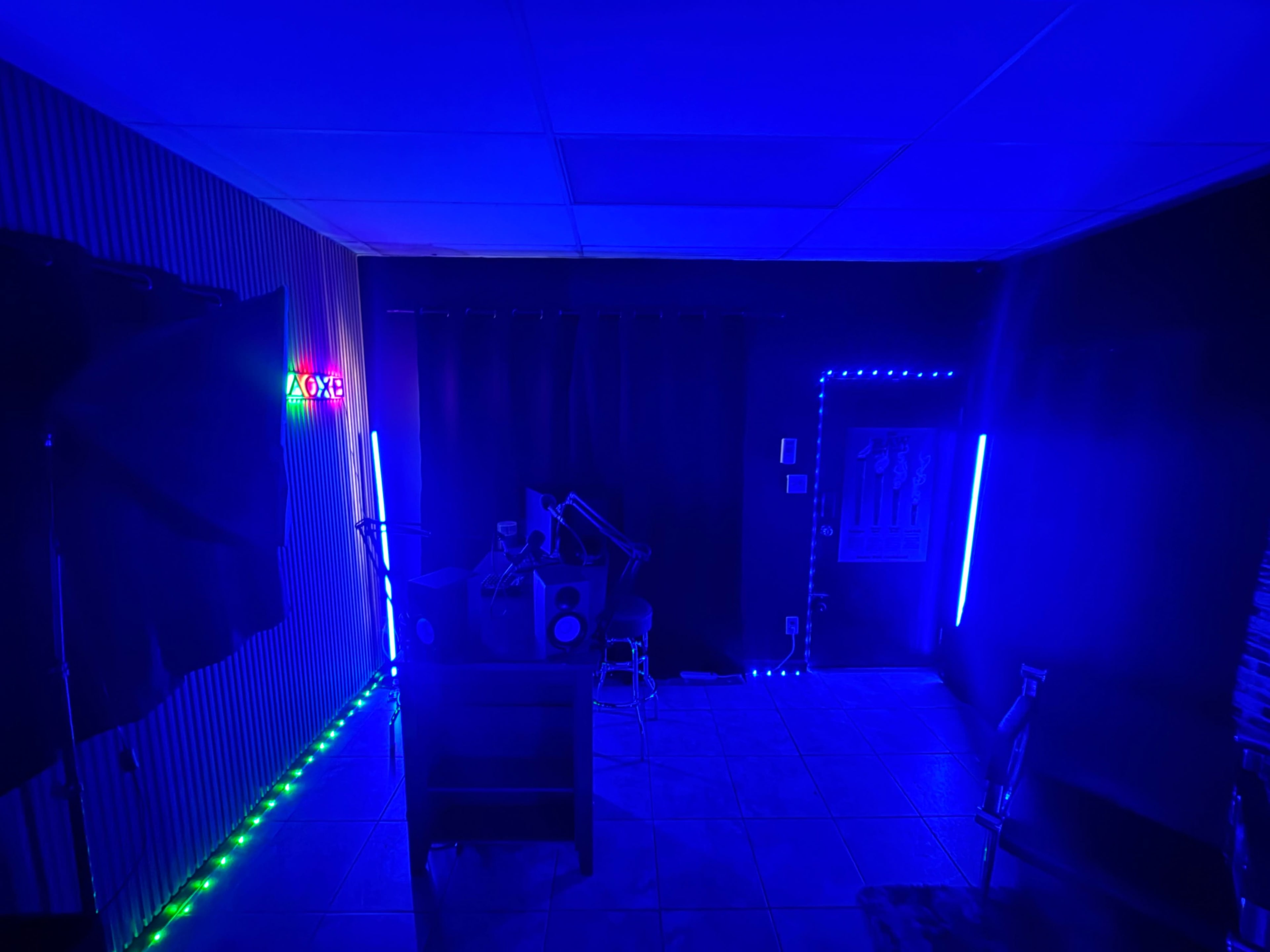 The image shows a dimly lit room with blue and green LED lights, featuring a desk with equipment and a curtain in the background.
