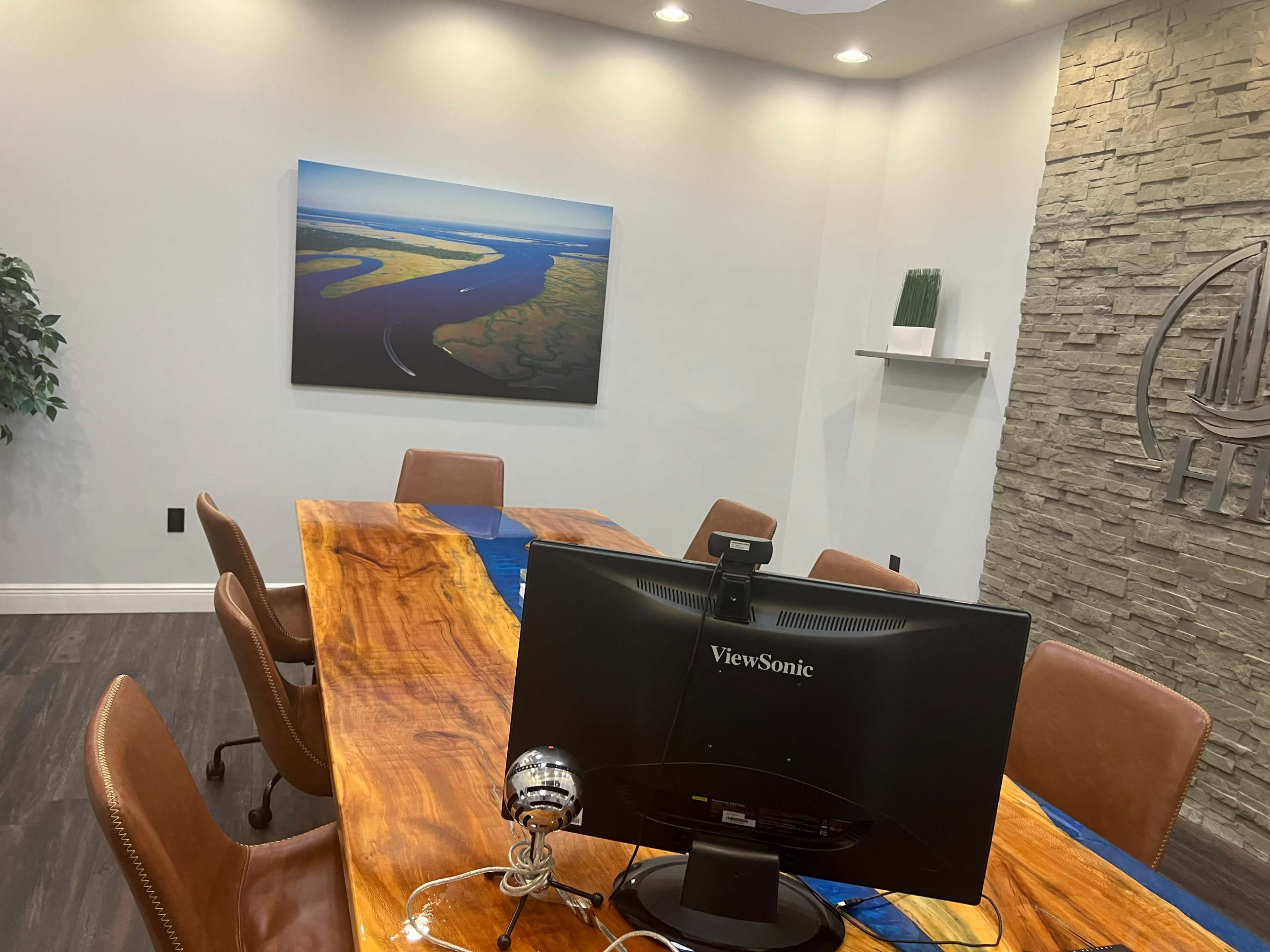 A conference room features a wooden table, a computer monitor, and a landscape artwork on the wall.