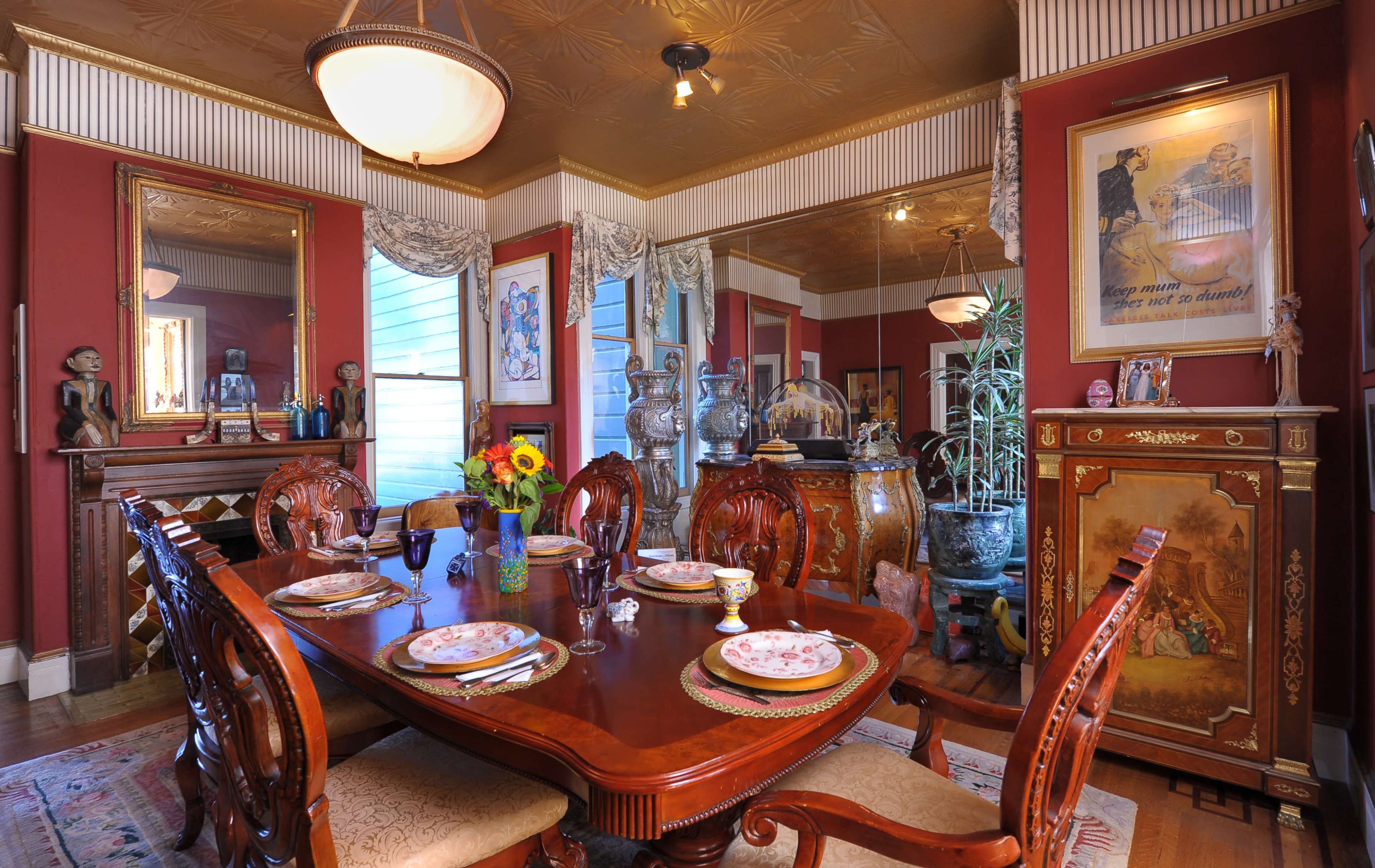A richly decorated dining room features a wooden table set for a meal, surrounded by ornate chairs and adorned with colorful floral arrangements and elegant tableware.
