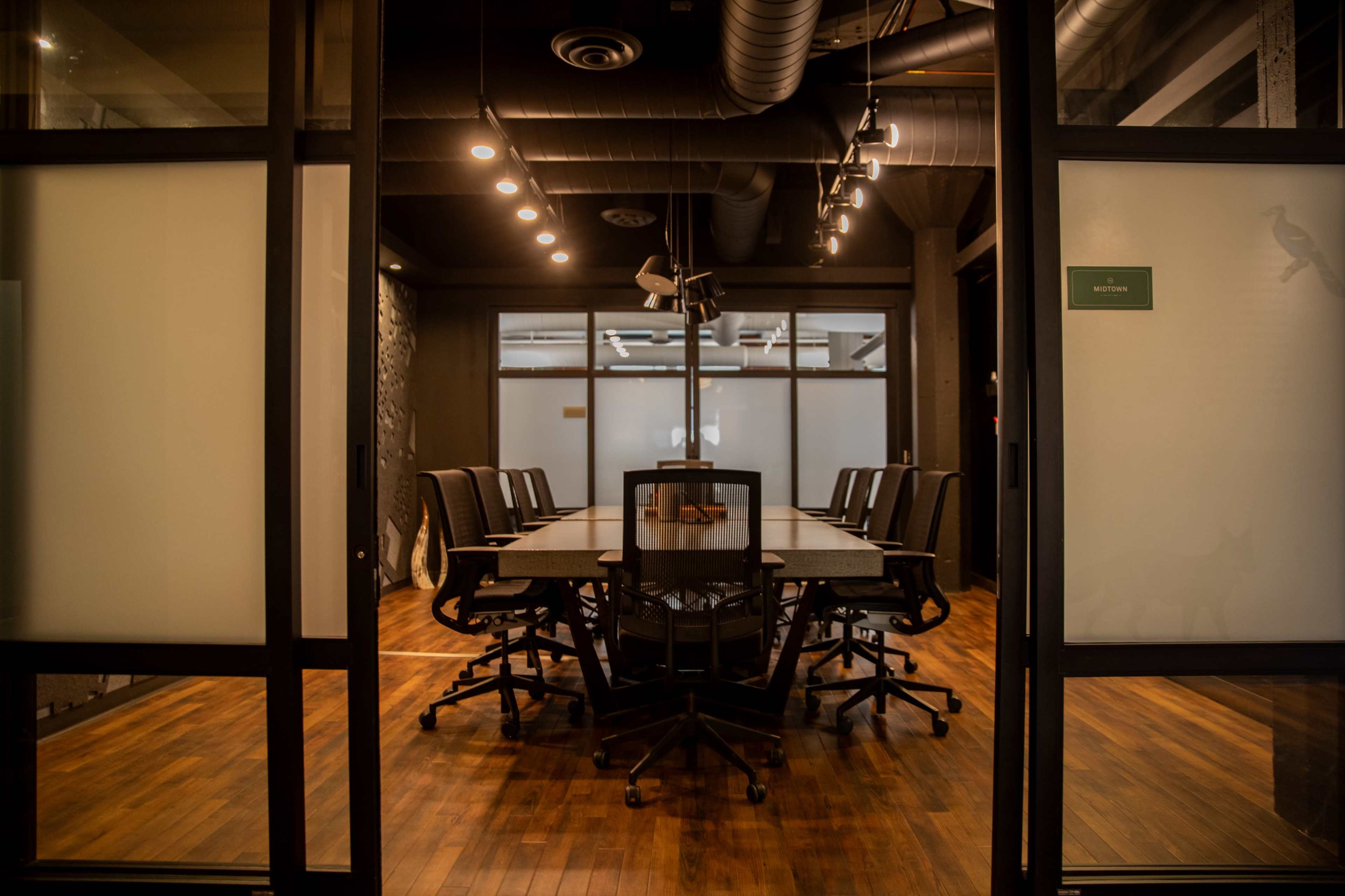 The image shows a modern conference room with a large table surrounded by office chairs and glass walls.