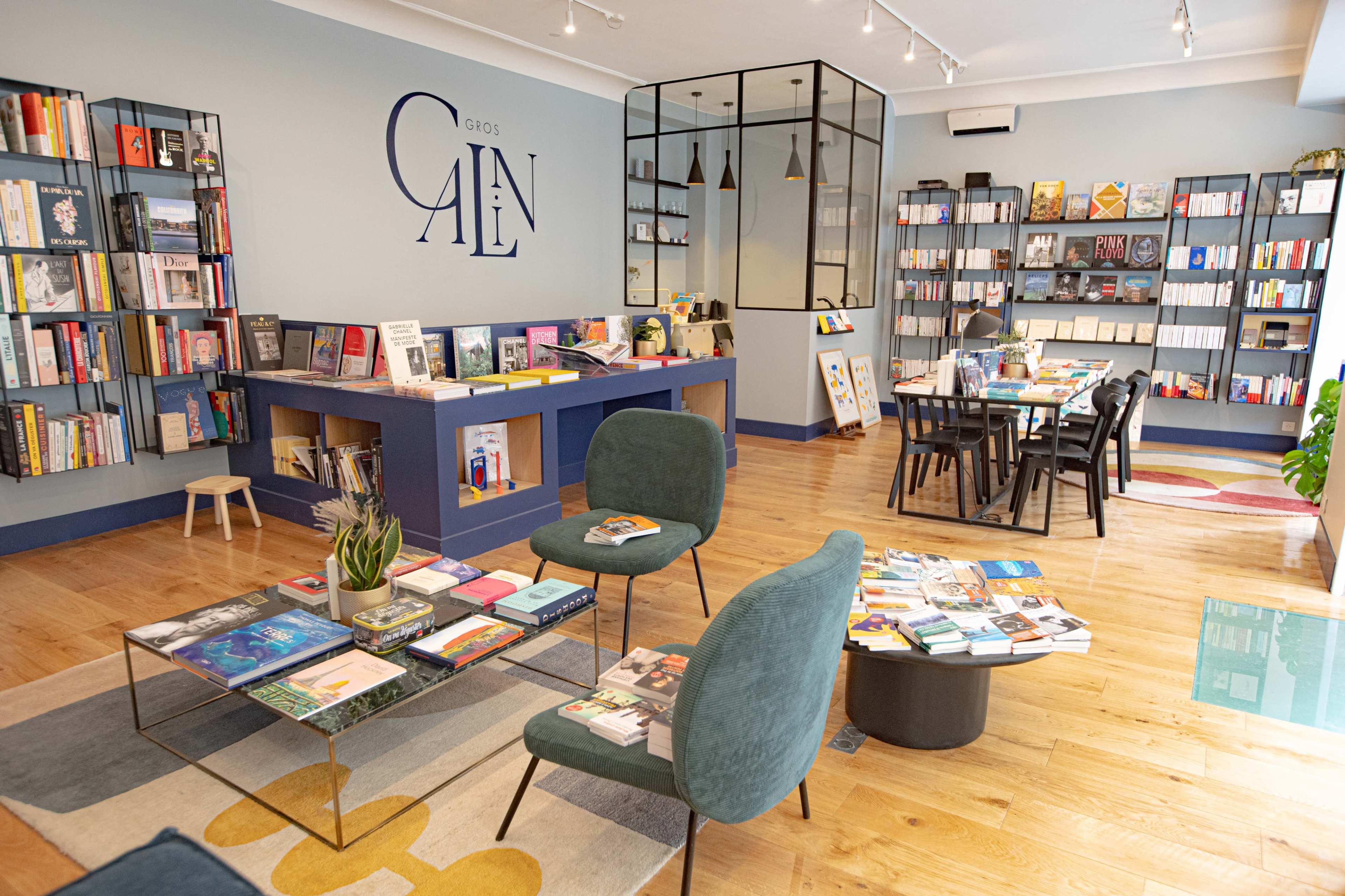 A modern bookstore interior with bookshelves lined with various titles, tables for reading, and a seating area featuring green chairs.