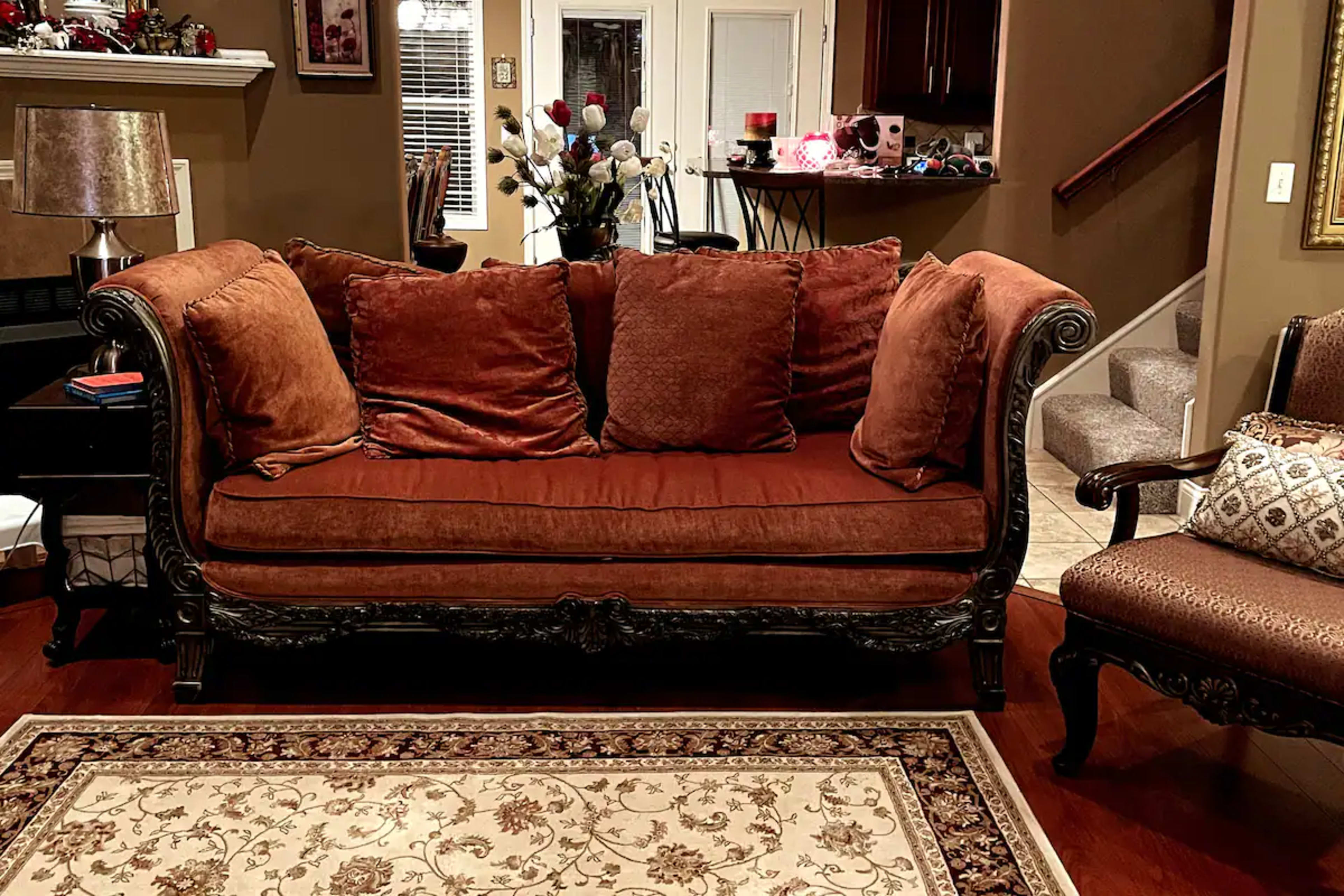 A brown sofa with large cushions, ornate wooden legs, placed on a patterned area rug in a warmly lit living room.