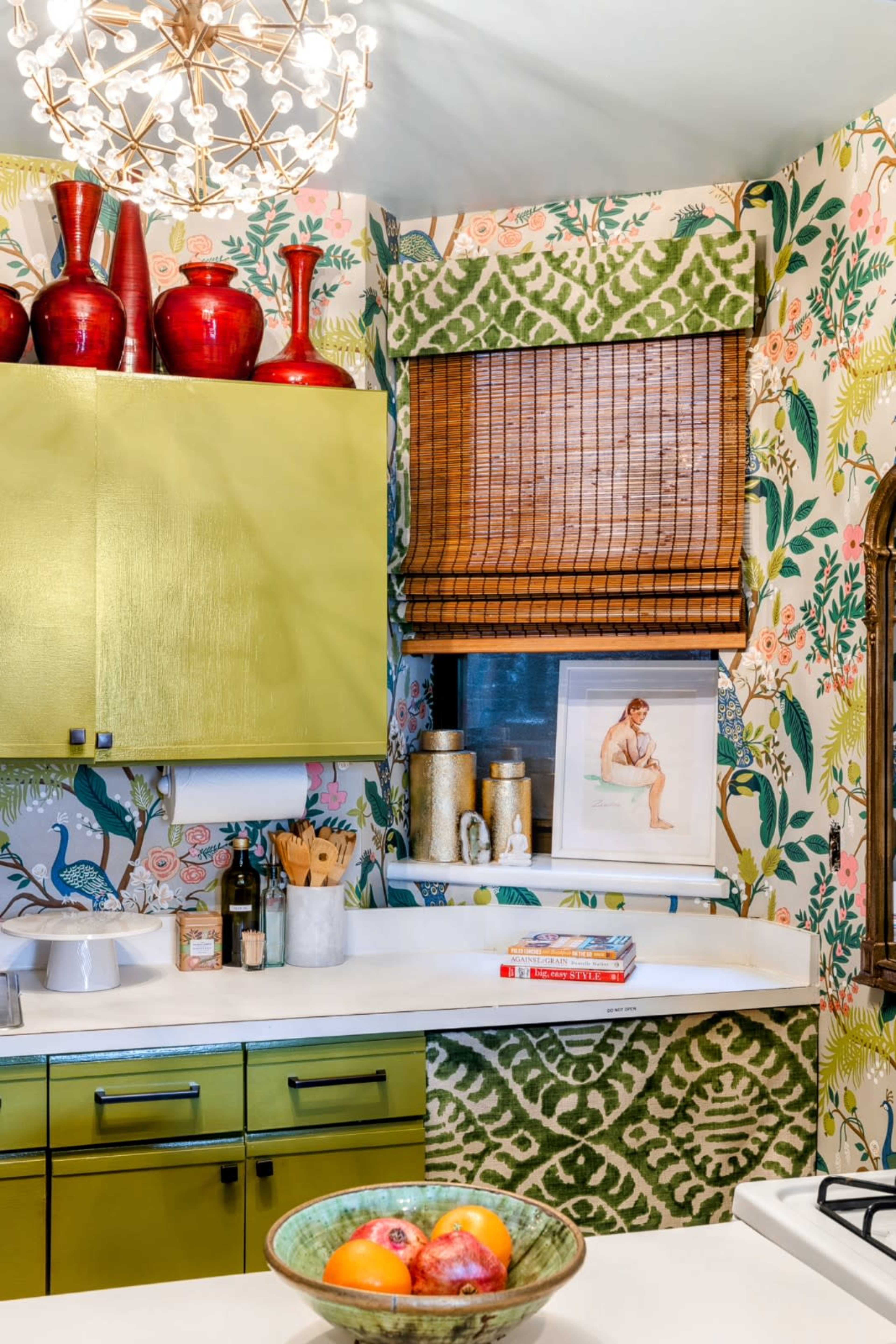 A brightly decorated kitchen features green cabinets, floral wallpaper, and a variety of decorative items on the countertops.